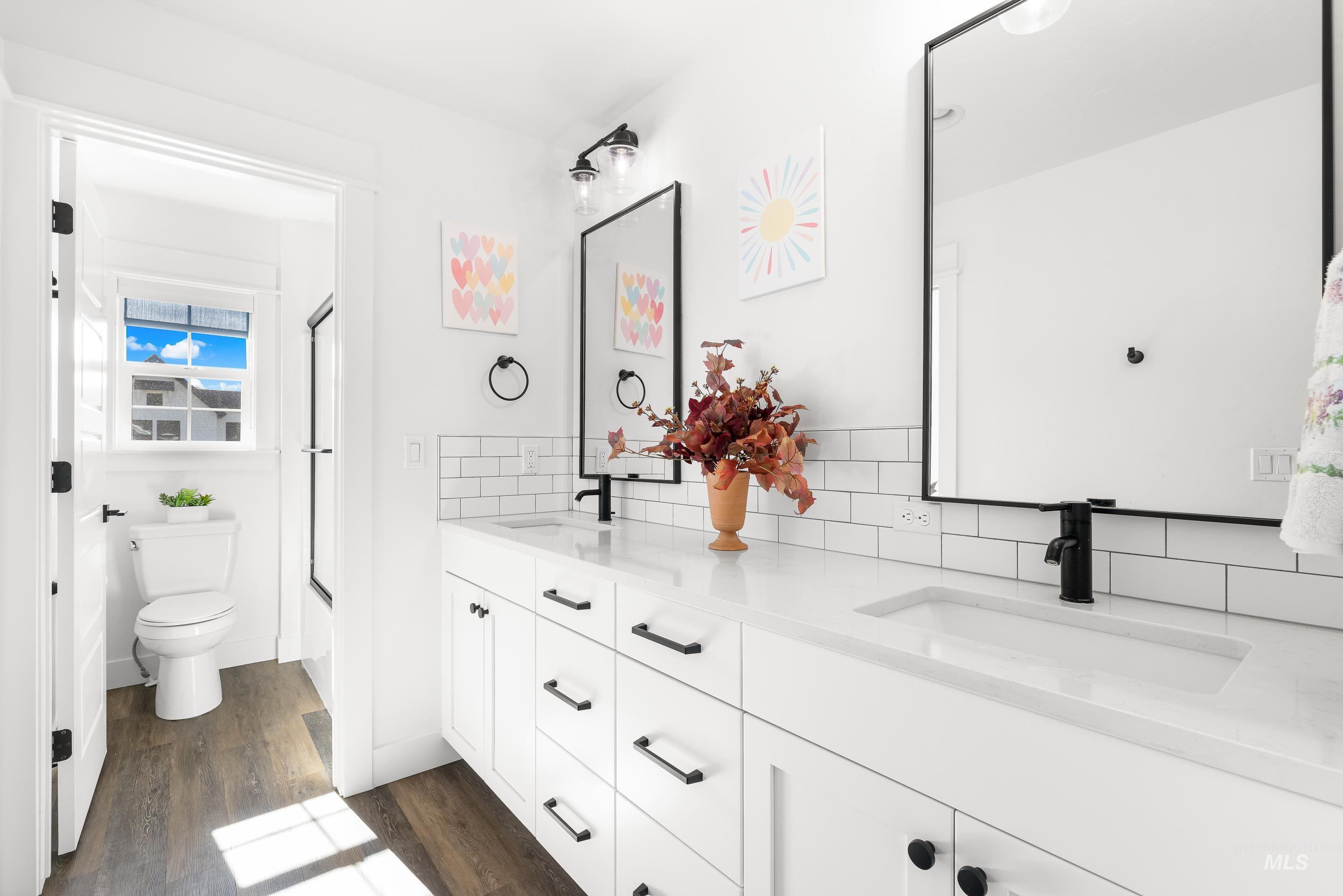 Bathroom with double vanity, backsplash, dark wood-style floors, and combined bath / shower with glass door