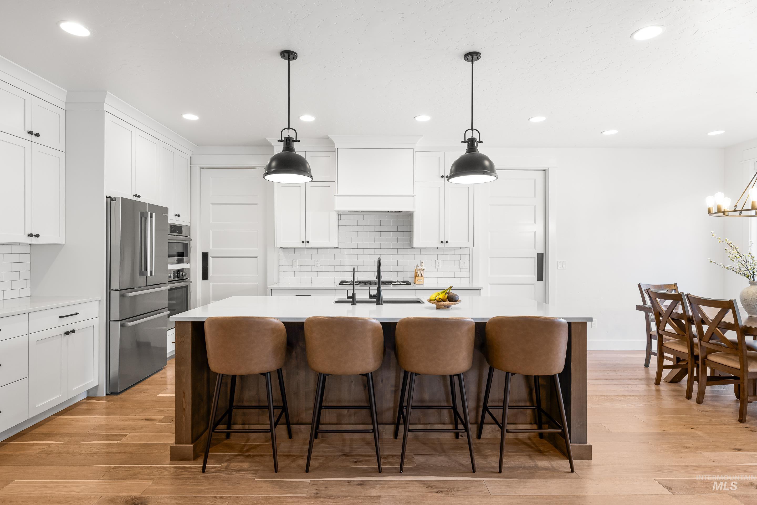 Kitchen with white cabinets, stainless steel appliances, decorative light fixtures, a kitchen island with sink, and a breakfast bar area