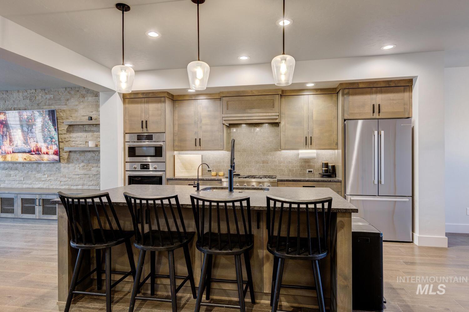 Kitchen featuring appliances with stainless steel finishes, light wood-style floors, an island with sink, hanging light fixtures, and recessed lighting