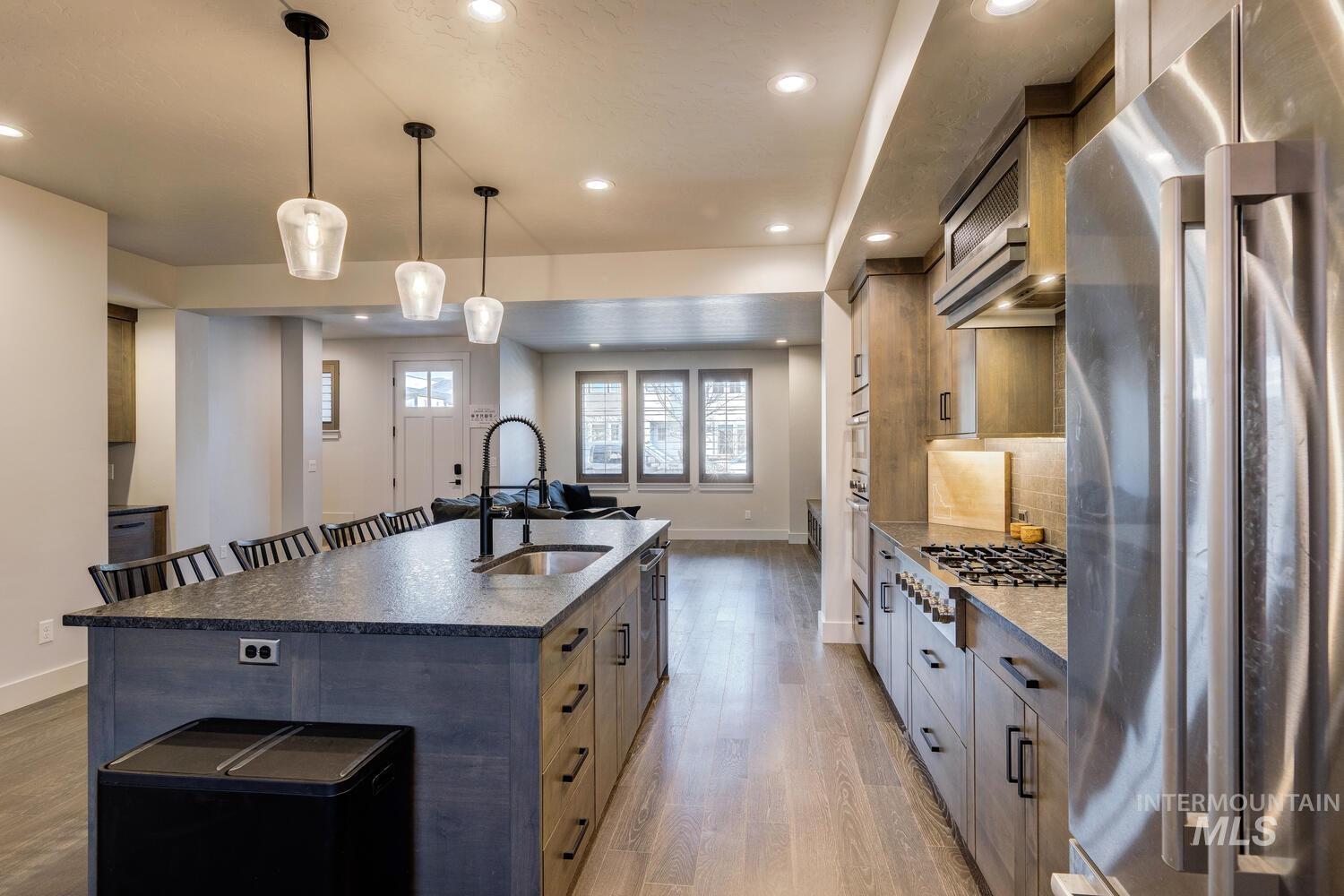 Kitchen with stainless steel appliances, decorative light fixtures, dark stone counters, light wood-style floors, and a spacious island