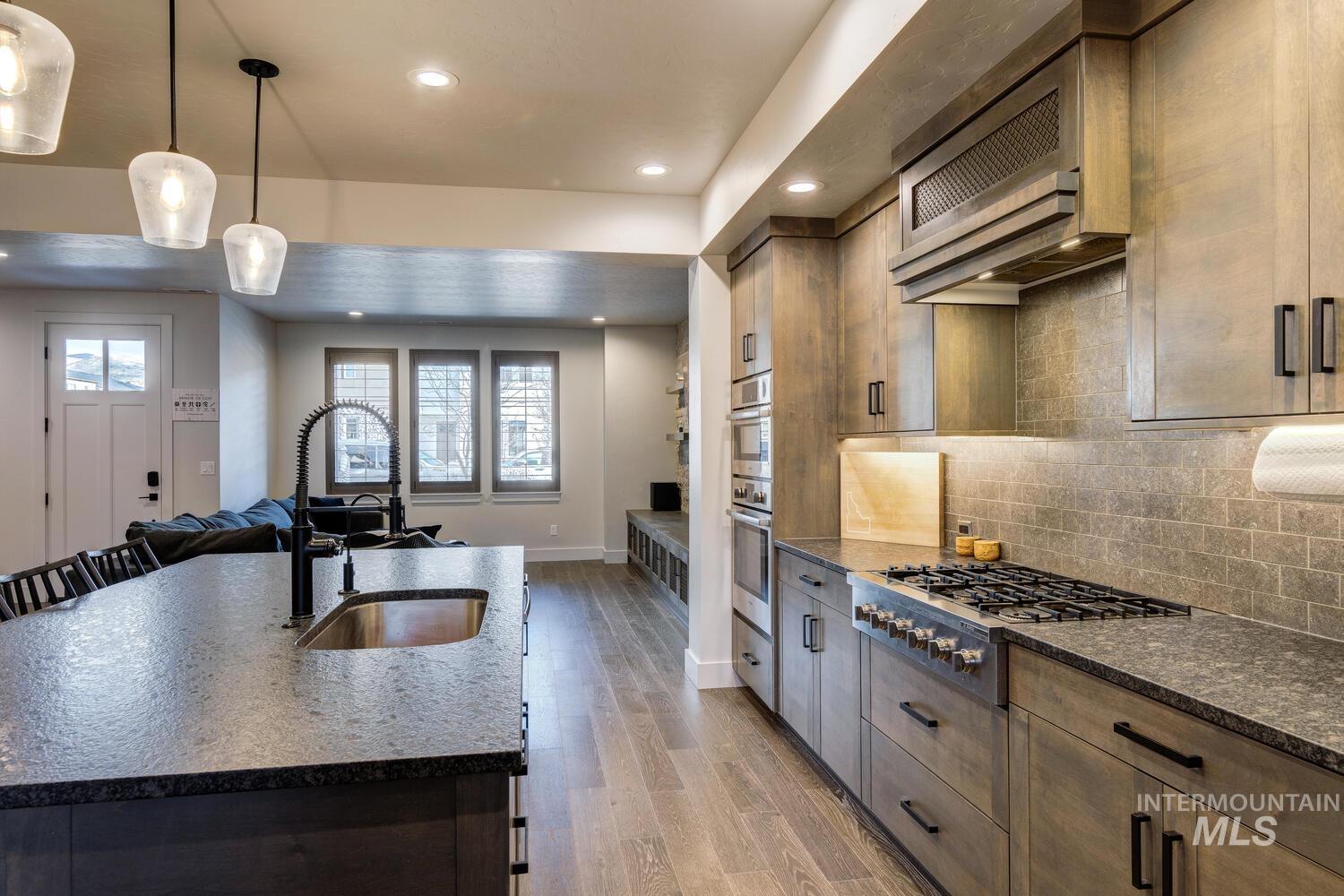 Kitchen featuring decorative light fixtures, open floor plan, appliances with stainless steel finishes, light wood-style flooring, and dark stone countertops