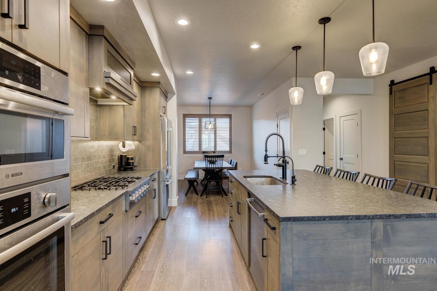 Kitchen featuring a barn door, appliances with stainless steel finishes, decorative light fixtures, a large island with sink, and dark stone countertops