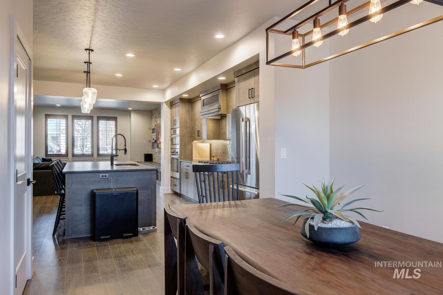 Kitchen with an island with sink, freestanding refrigerator, dark wood-style flooring, recessed lighting, and dark stone countertops