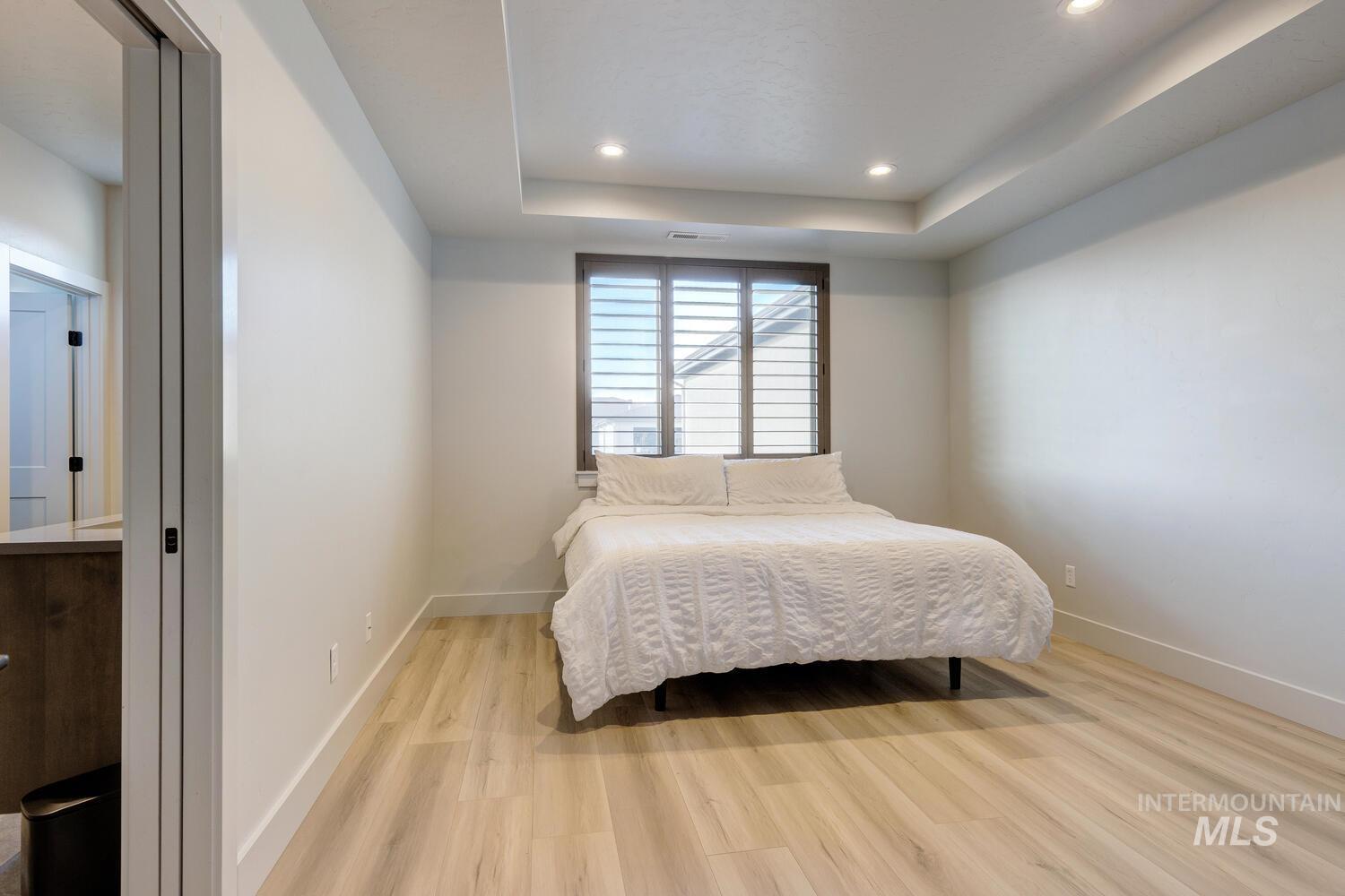 Bedroom with wood finished floors, a tray ceiling, and recessed lighting