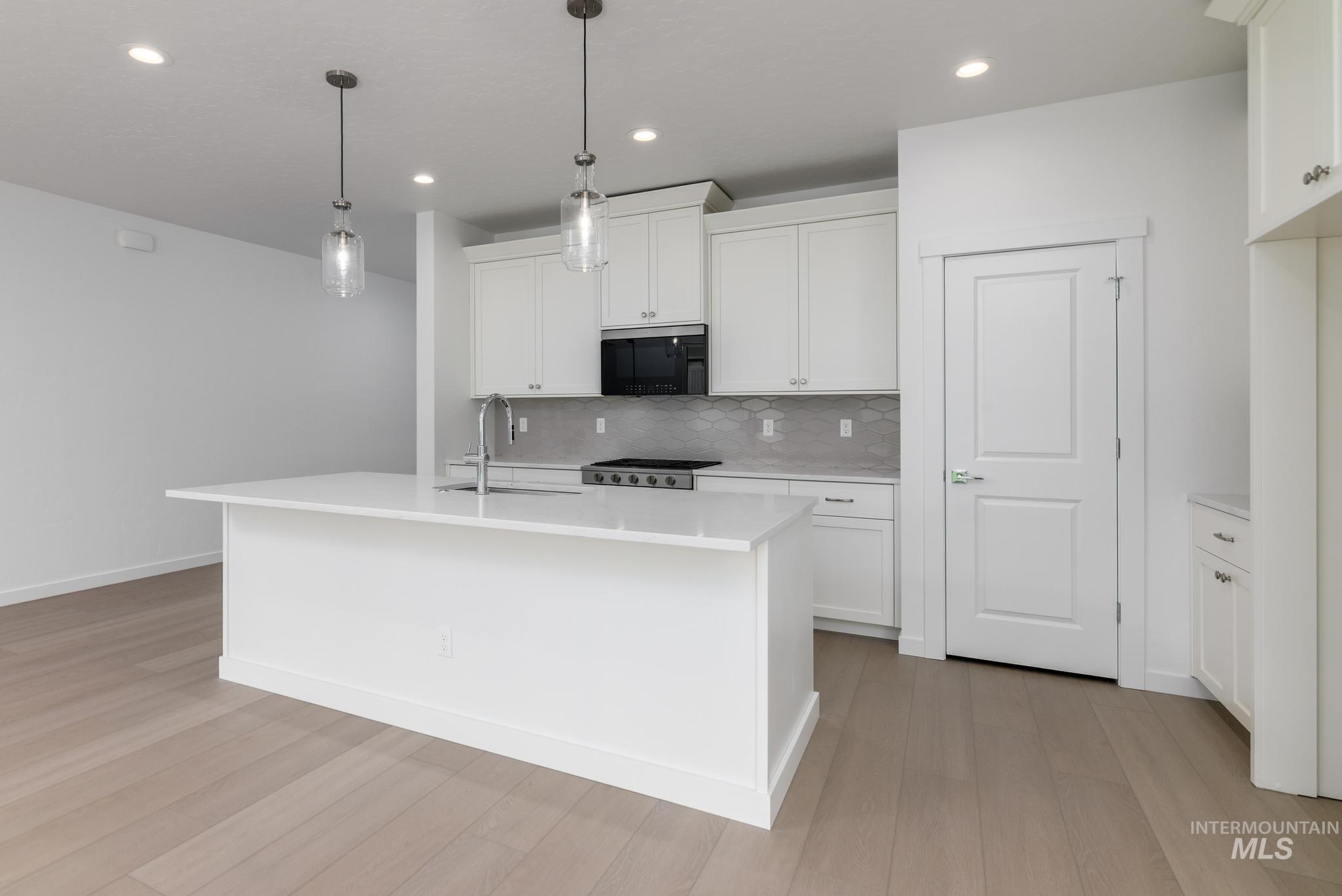 Kitchen with decorative light fixtures, white cabinetry, a kitchen island with sink, backsplash, and stainless steel gas range oven