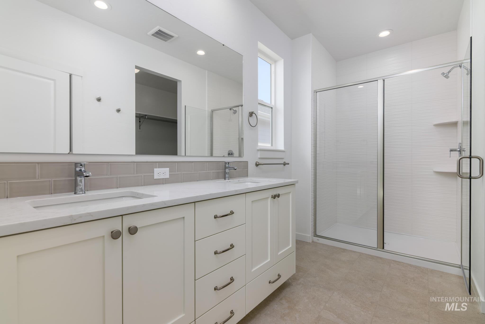 Full bathroom with double vanity, backsplash, a stall shower, a walk in closet, and recessed lighting