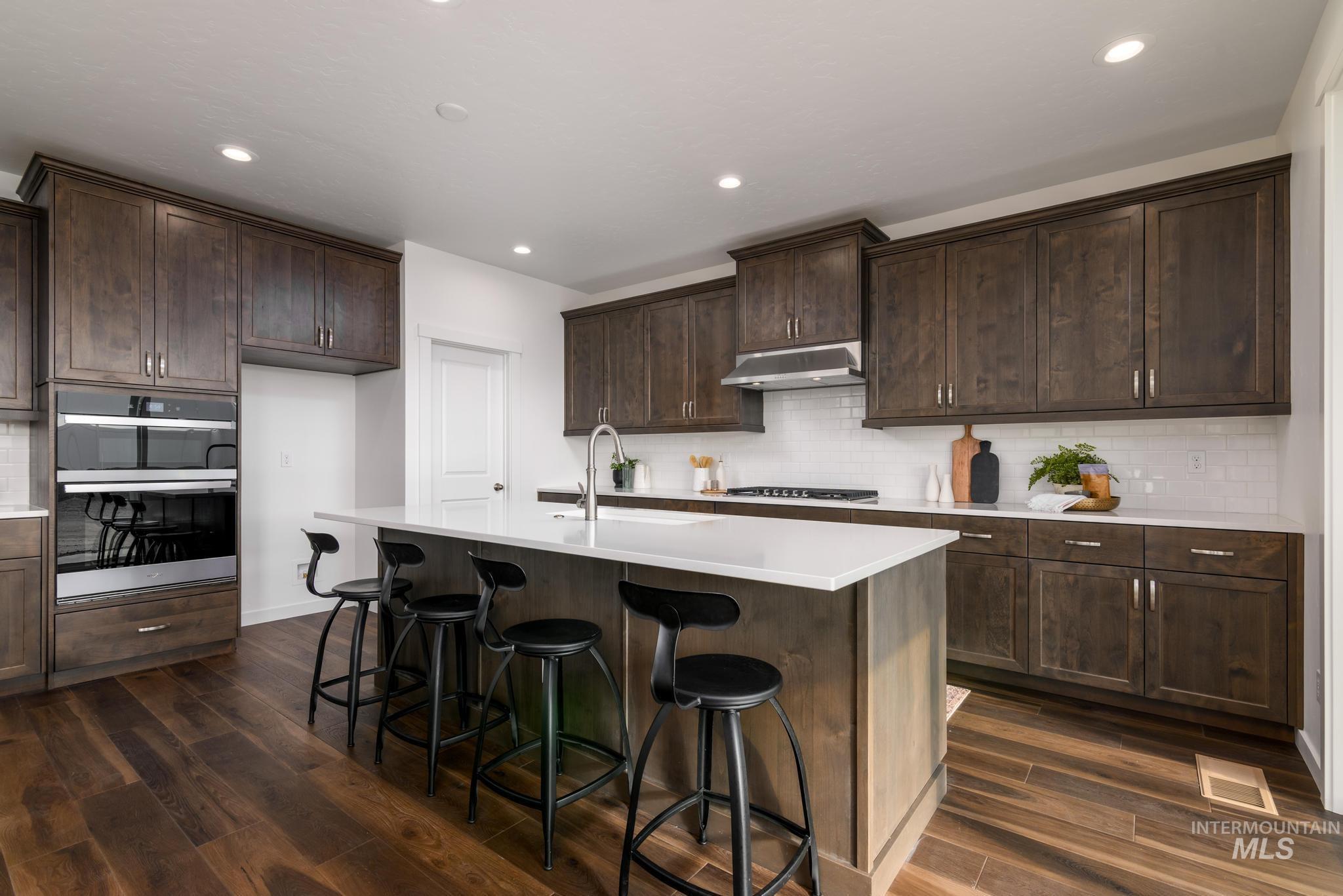 Kitchen with dark wood-type flooring, double oven, dark brown cabinetry, a breakfast bar, and decorative backsplash