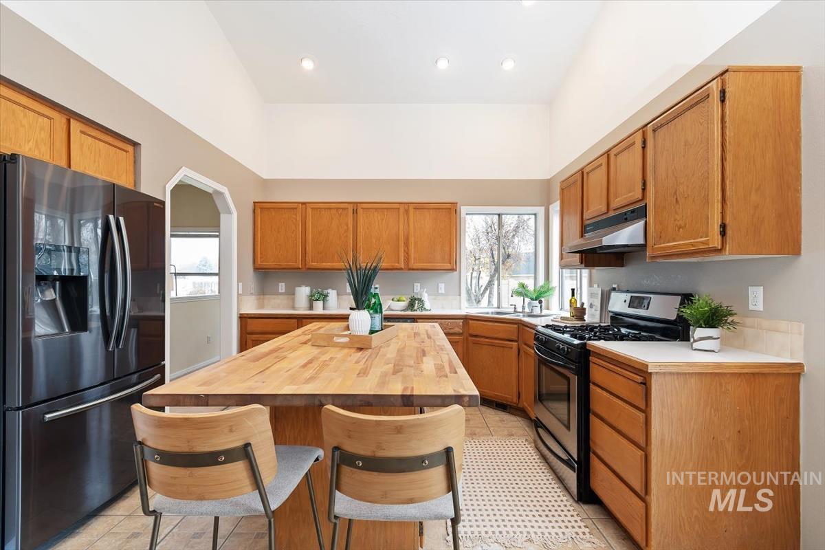 Kitchen featuring black fridge, gas stove, brown cabinets, a breakfast bar area, and under cabinet range hood