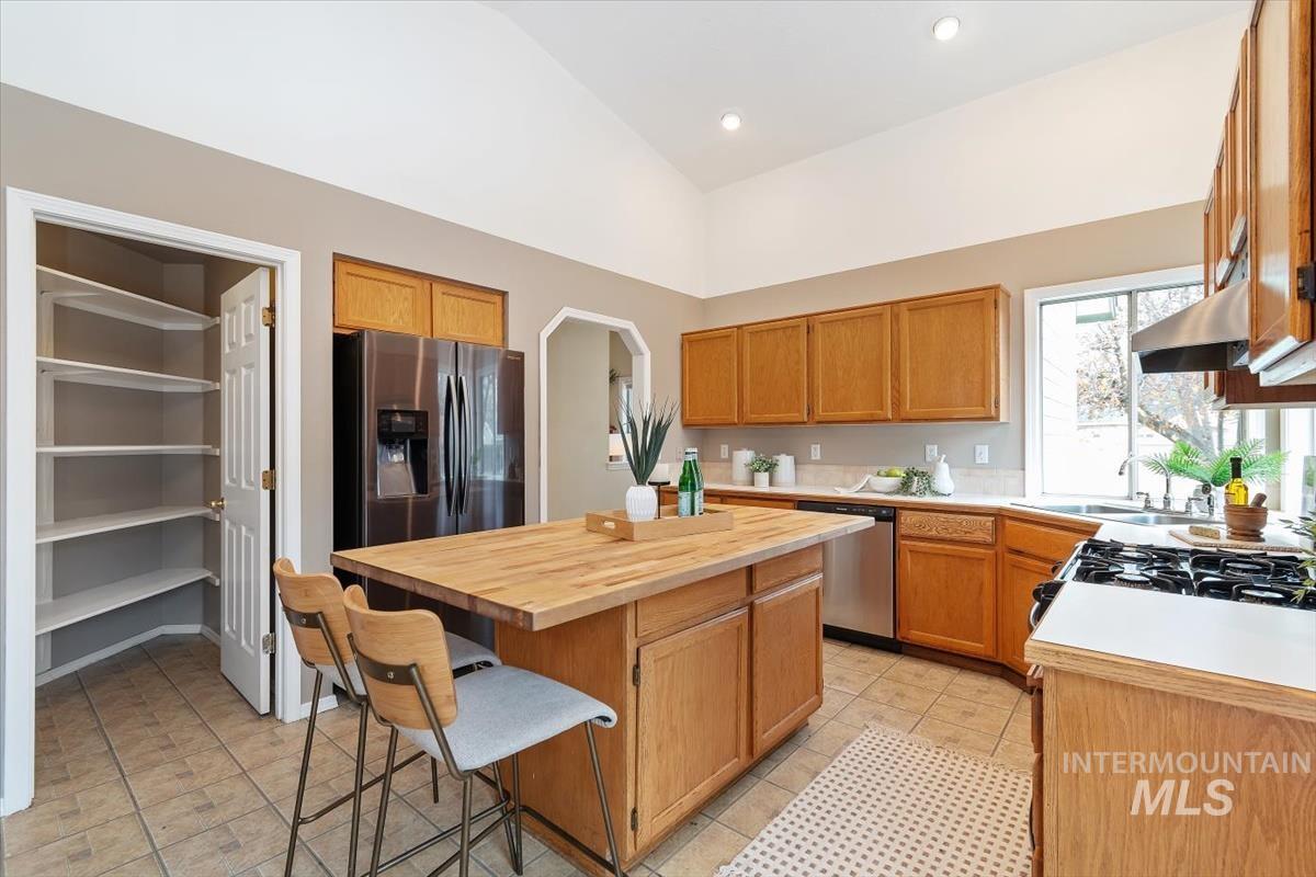 Kitchen featuring a breakfast bar, appliances with stainless steel finishes, a kitchen island, vaulted ceiling, and brown cabinetry