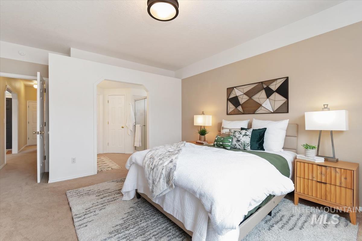 Bedroom featuring light carpet, arched walkways, and ensuite bath