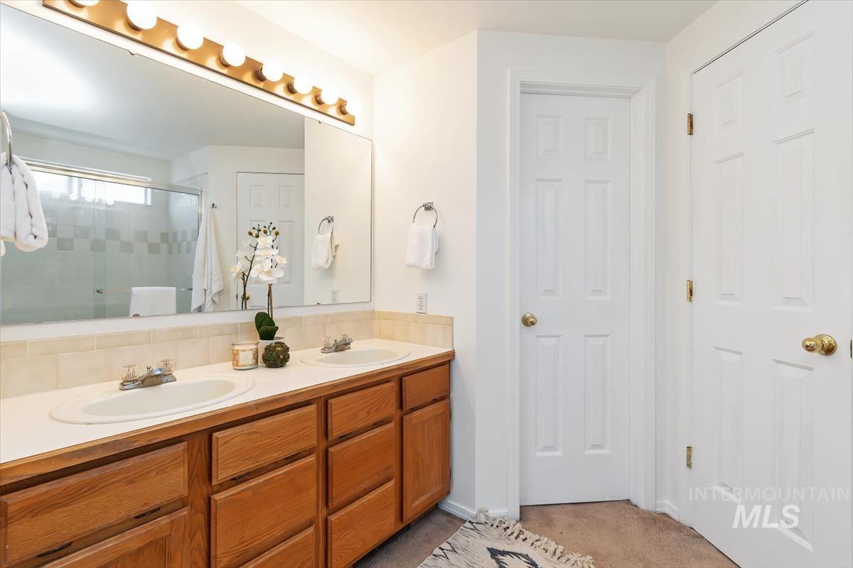 Full bathroom featuring double vanity, a shower stall, and light colored carpet