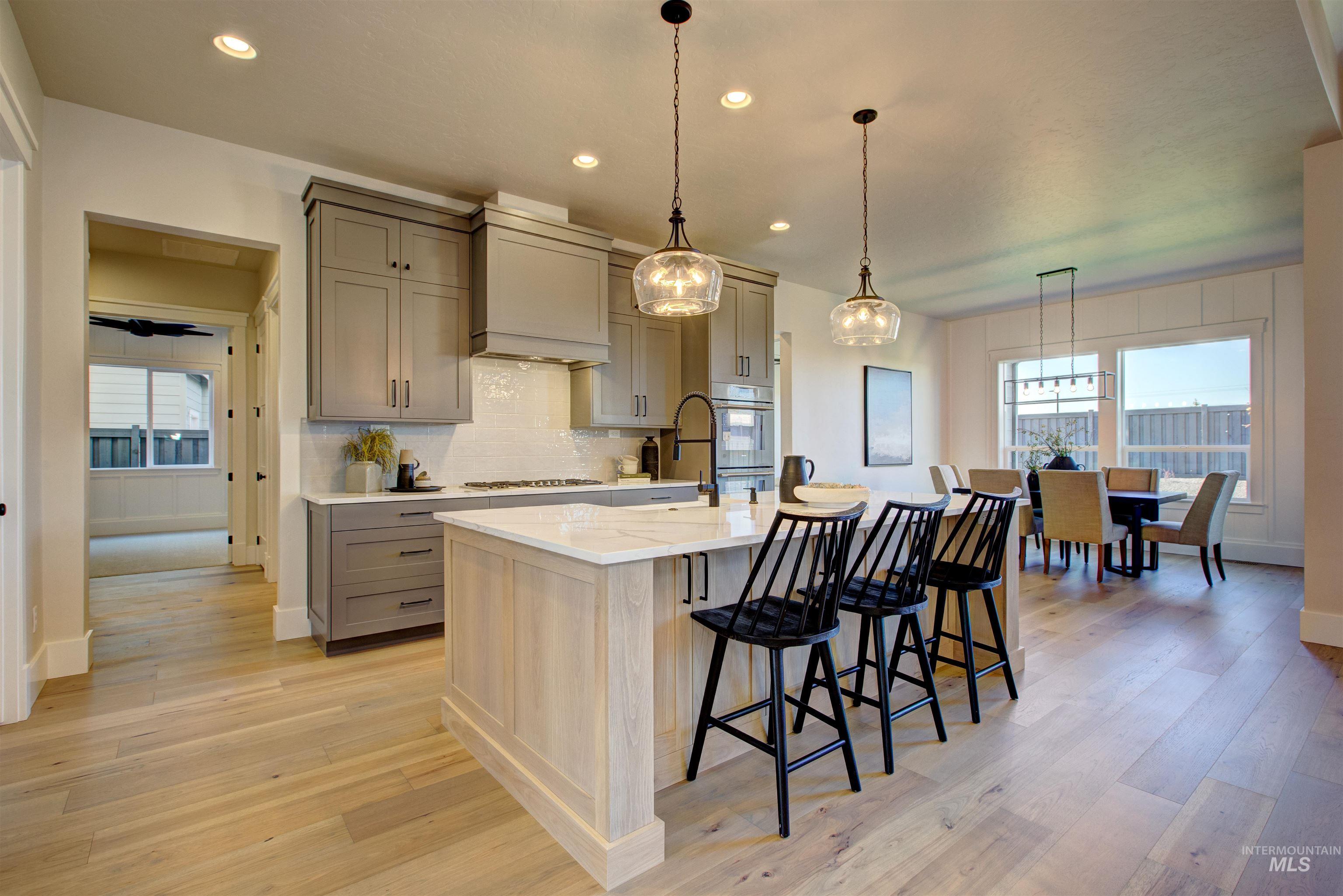 Kitchen featuring gray cabinetry, pendant lighting, backsplash, light stone countertops, and light wood-style flooring