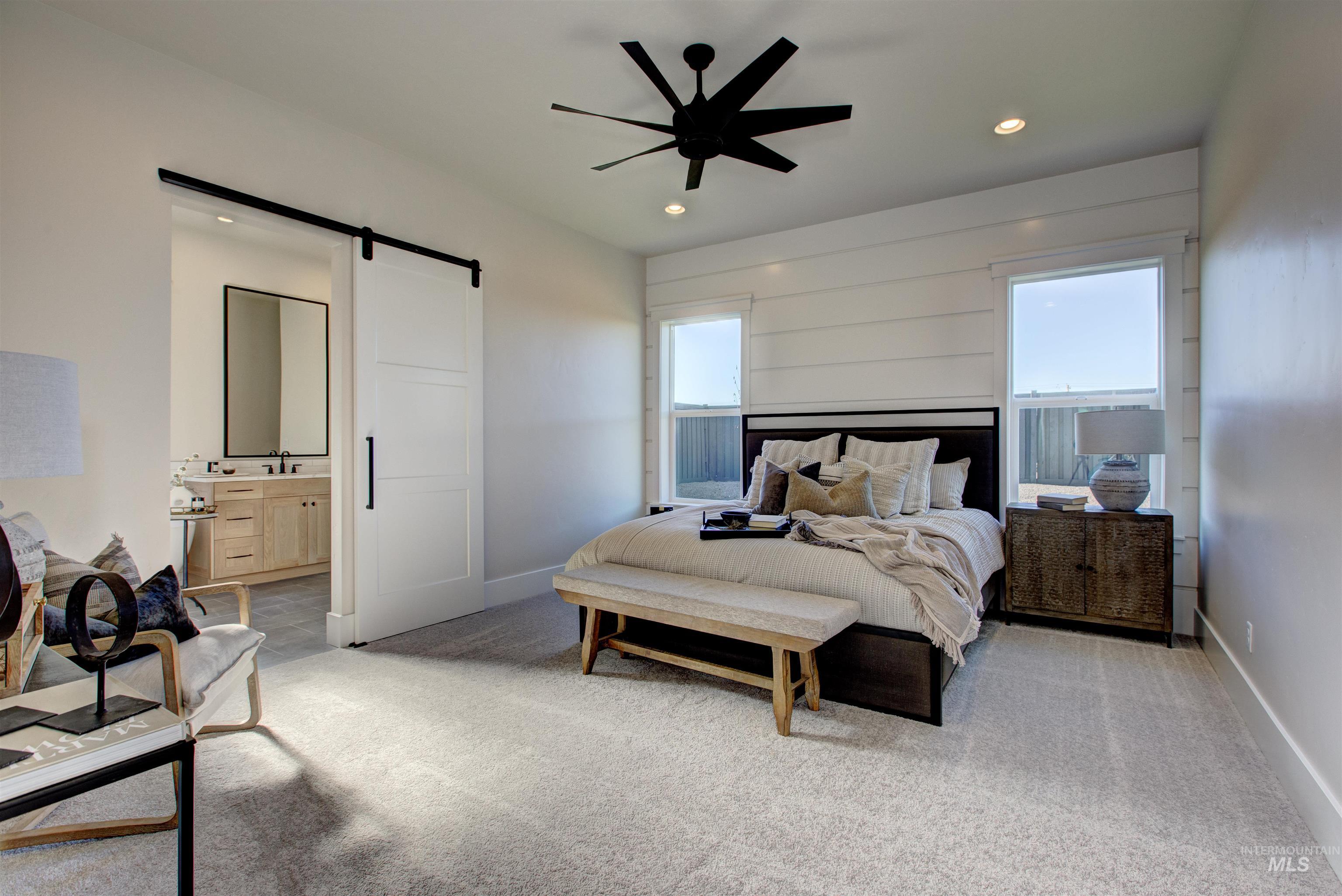 Bedroom with a barn door, light colored carpet, recessed lighting, a ceiling fan, and ensuite bathroom