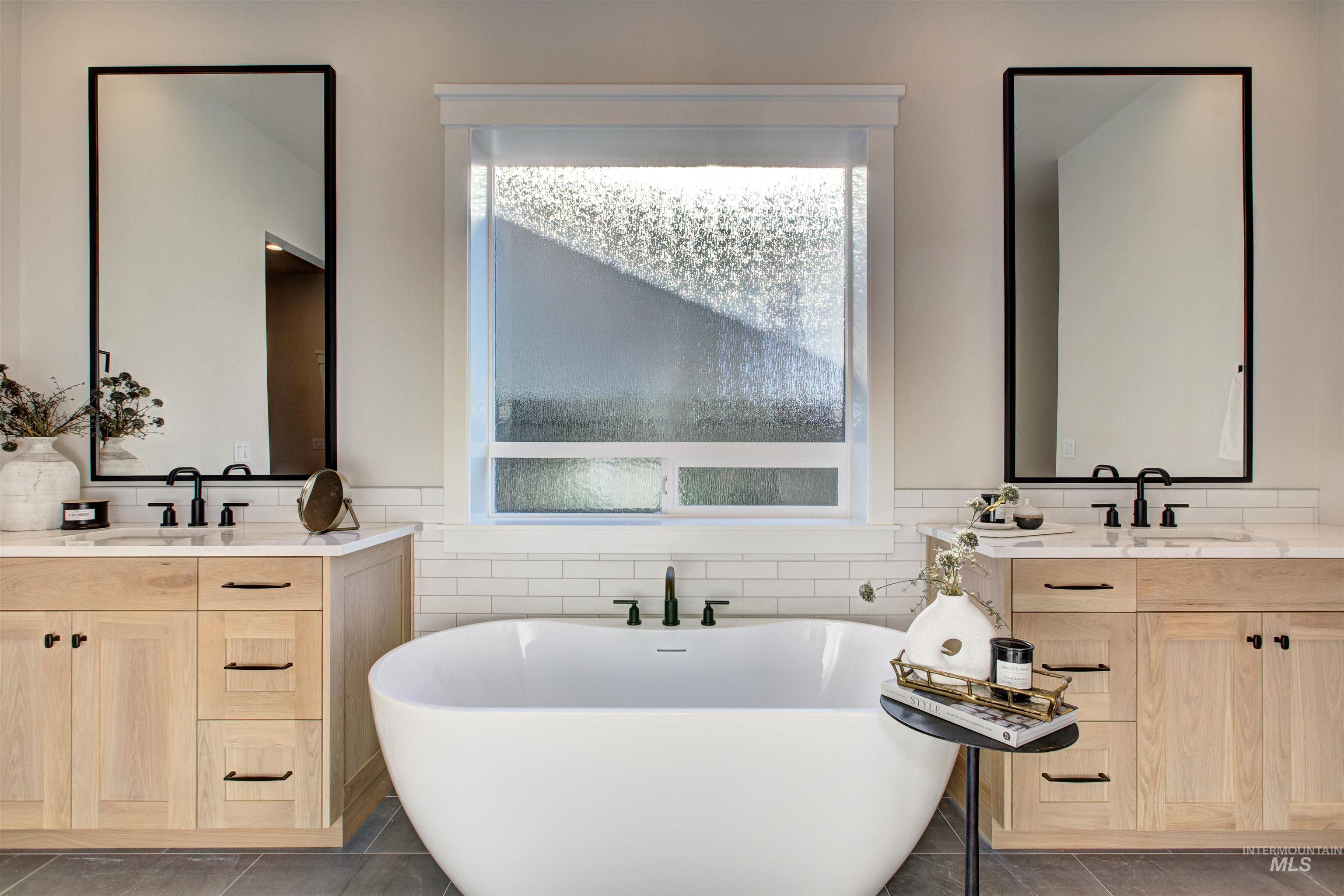 Full bathroom featuring two vanities, a freestanding bath, dark tile patterned floors, wainscoting, and tile walls