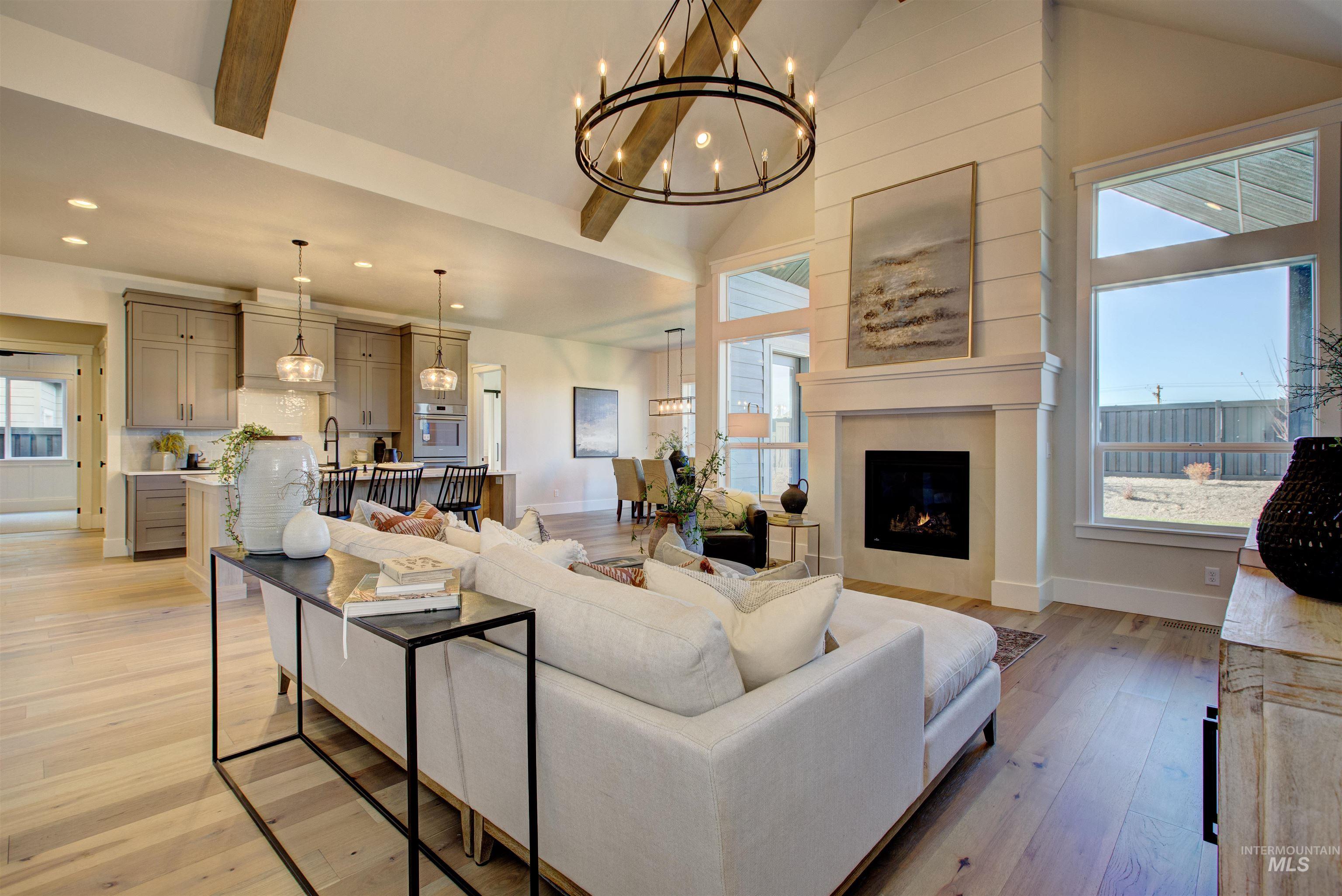 Living area featuring light wood-style flooring, a chandelier, high vaulted ceiling, and a lit fireplace