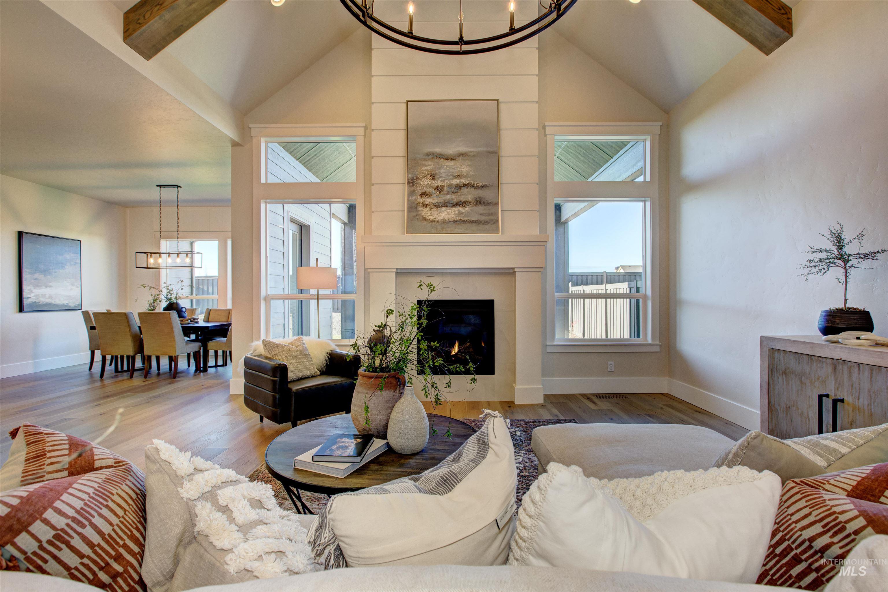 Living area with a chandelier, beam ceiling, wood finished floors, a large fireplace, and high vaulted ceiling