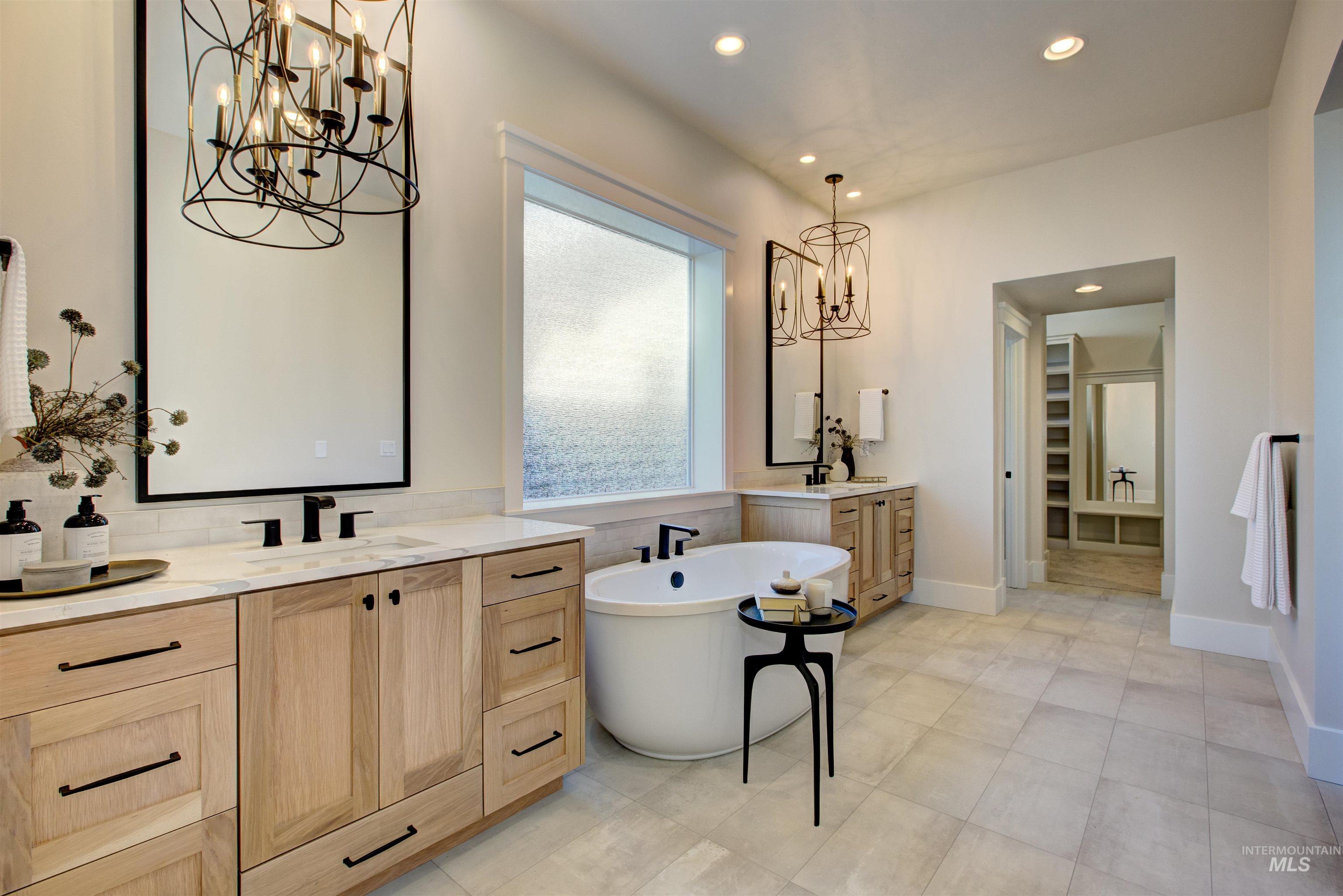 Full bath with a chandelier, two vanities, a soaking tub, and recessed lighting