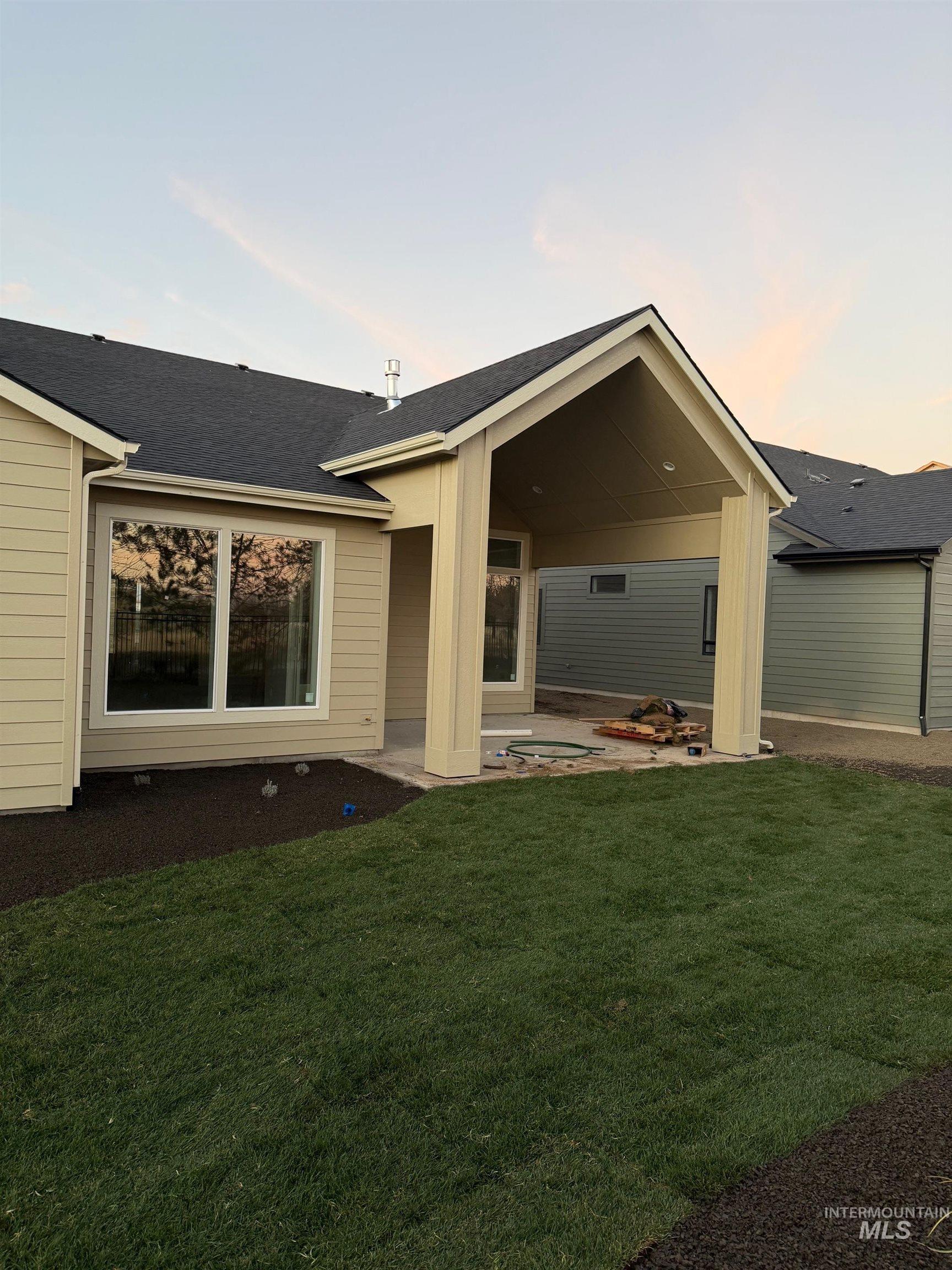 Back of house at dusk featuring a patio area, a yard, and roof with shingles