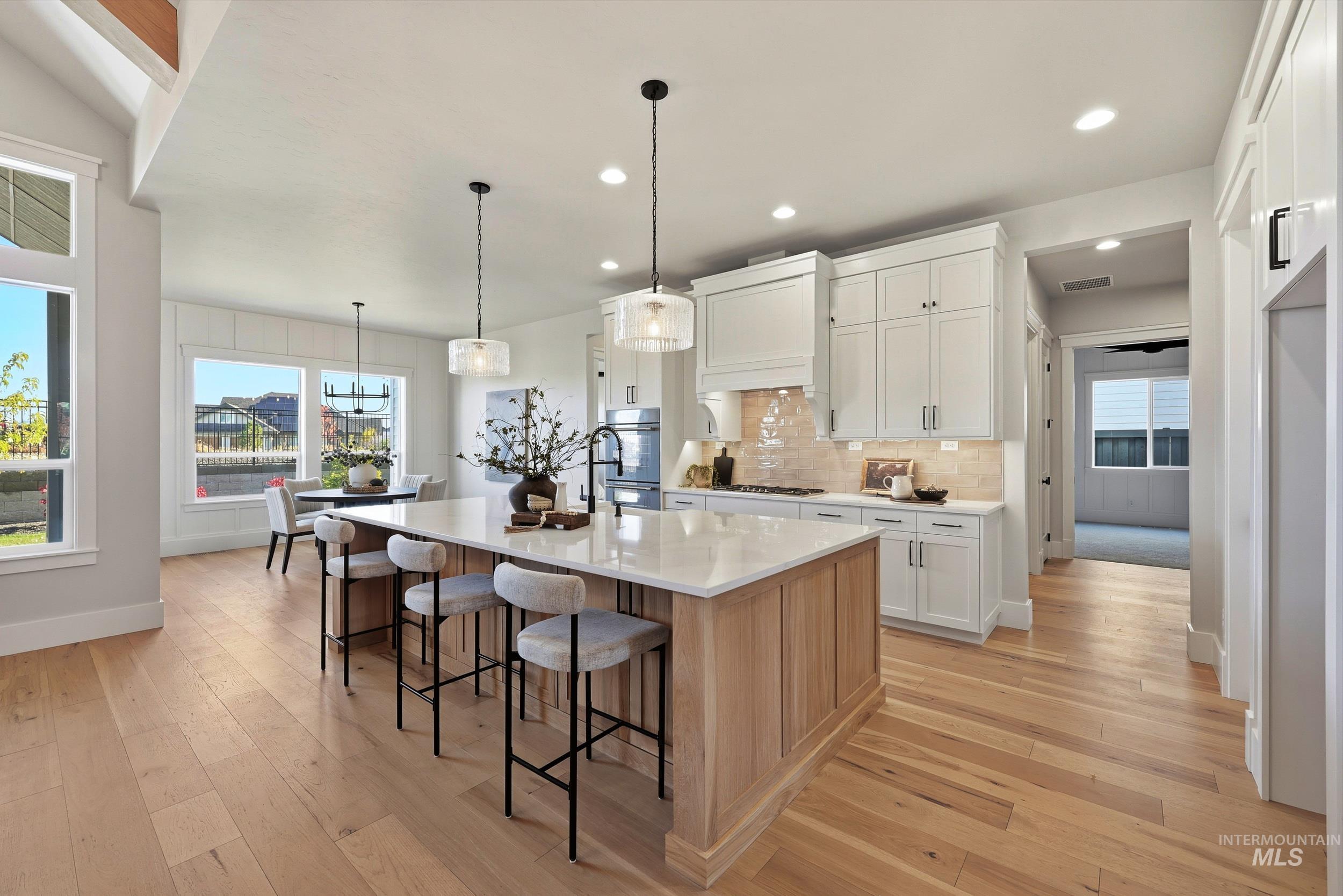 Kitchen with decorative backsplash, white cabinetry, a breakfast bar area, pendant lighting, and light wood-type flooring