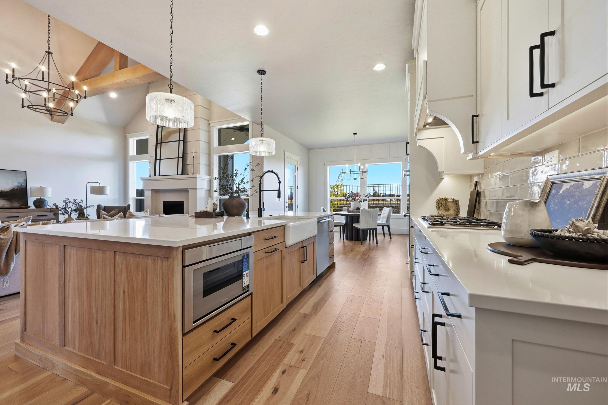 Kitchen featuring a chandelier, white cabinets, light wood finished floors, tasteful backsplash, and pendant lighting