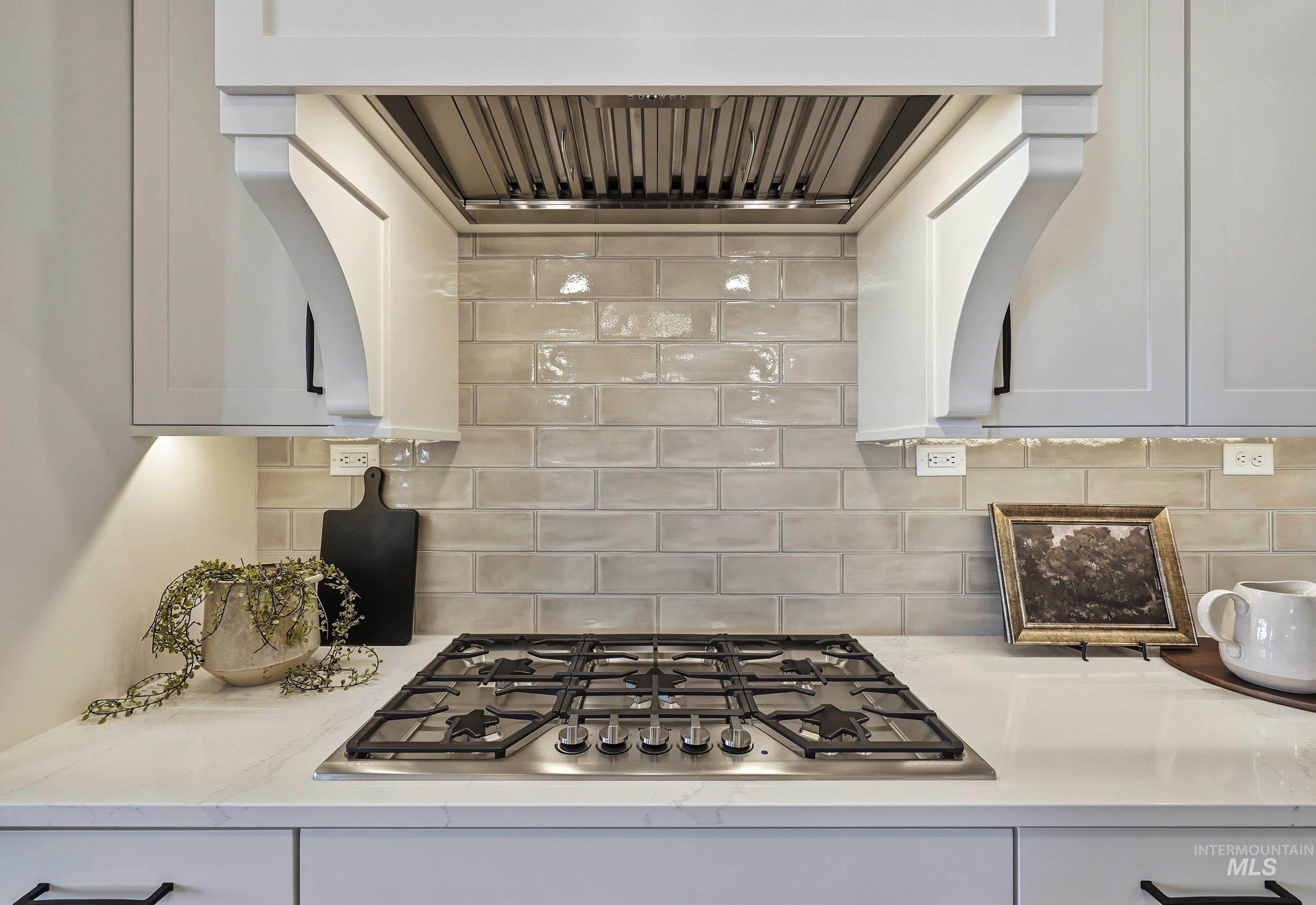 Kitchen featuring ventilation hood, stainless steel gas stovetop, backsplash, and white cabinets