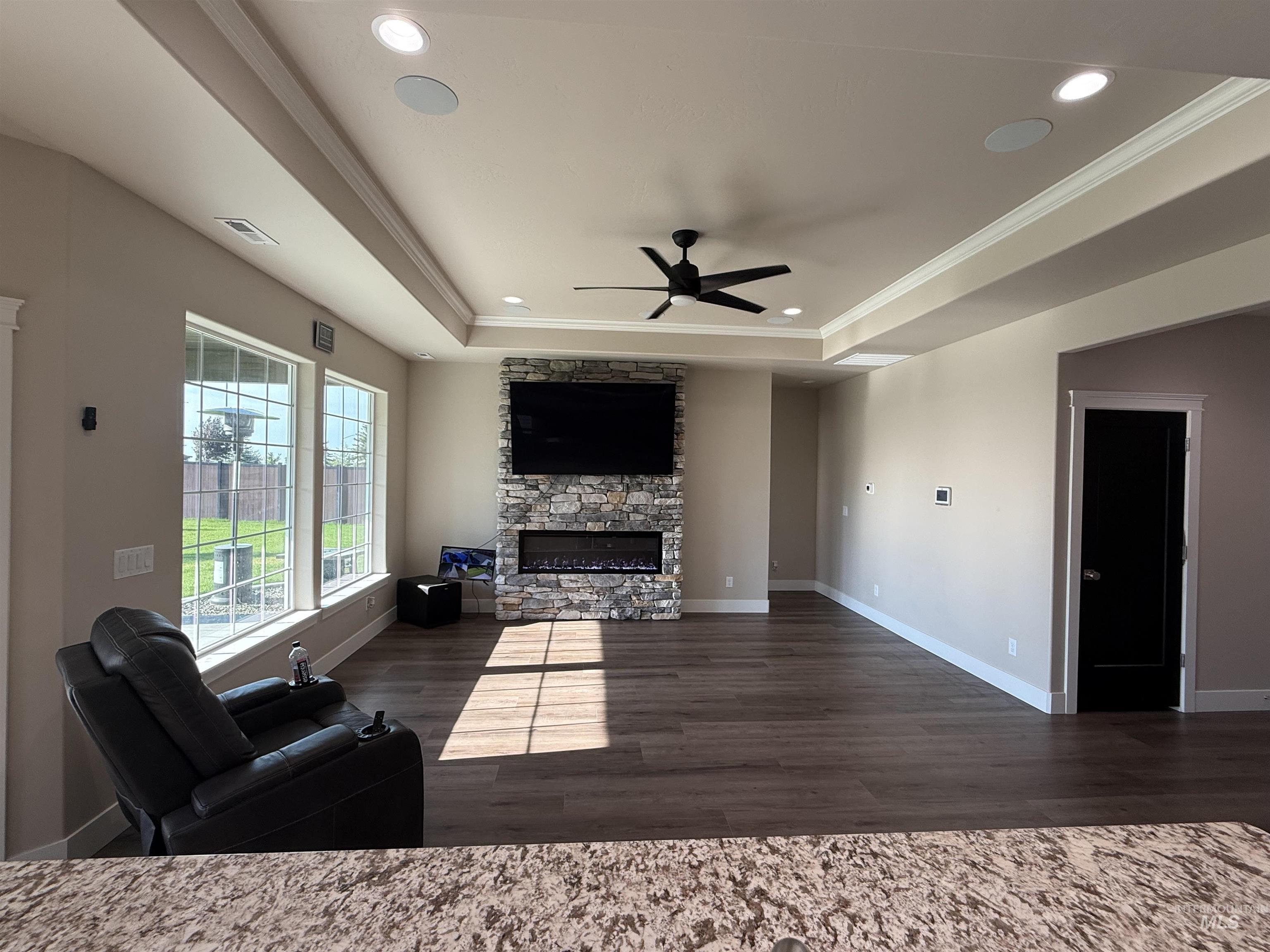 Living area featuring a stone fireplace, ceiling fan, dark wood finished floors, recessed lighting, and a tray ceiling
