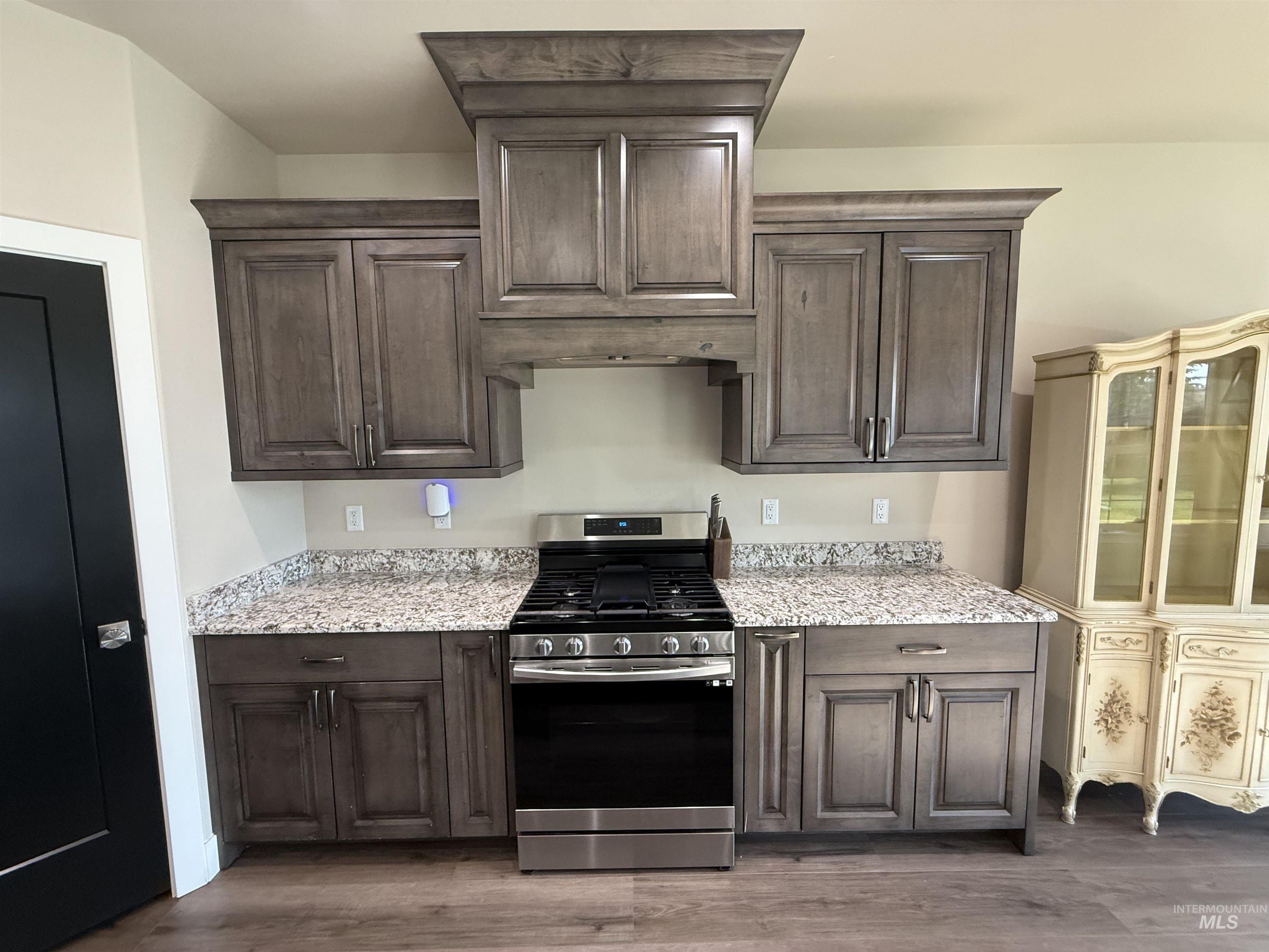 Kitchen featuring gas stove, dark brown cabinetry, light stone countertops, and dark wood finished floors