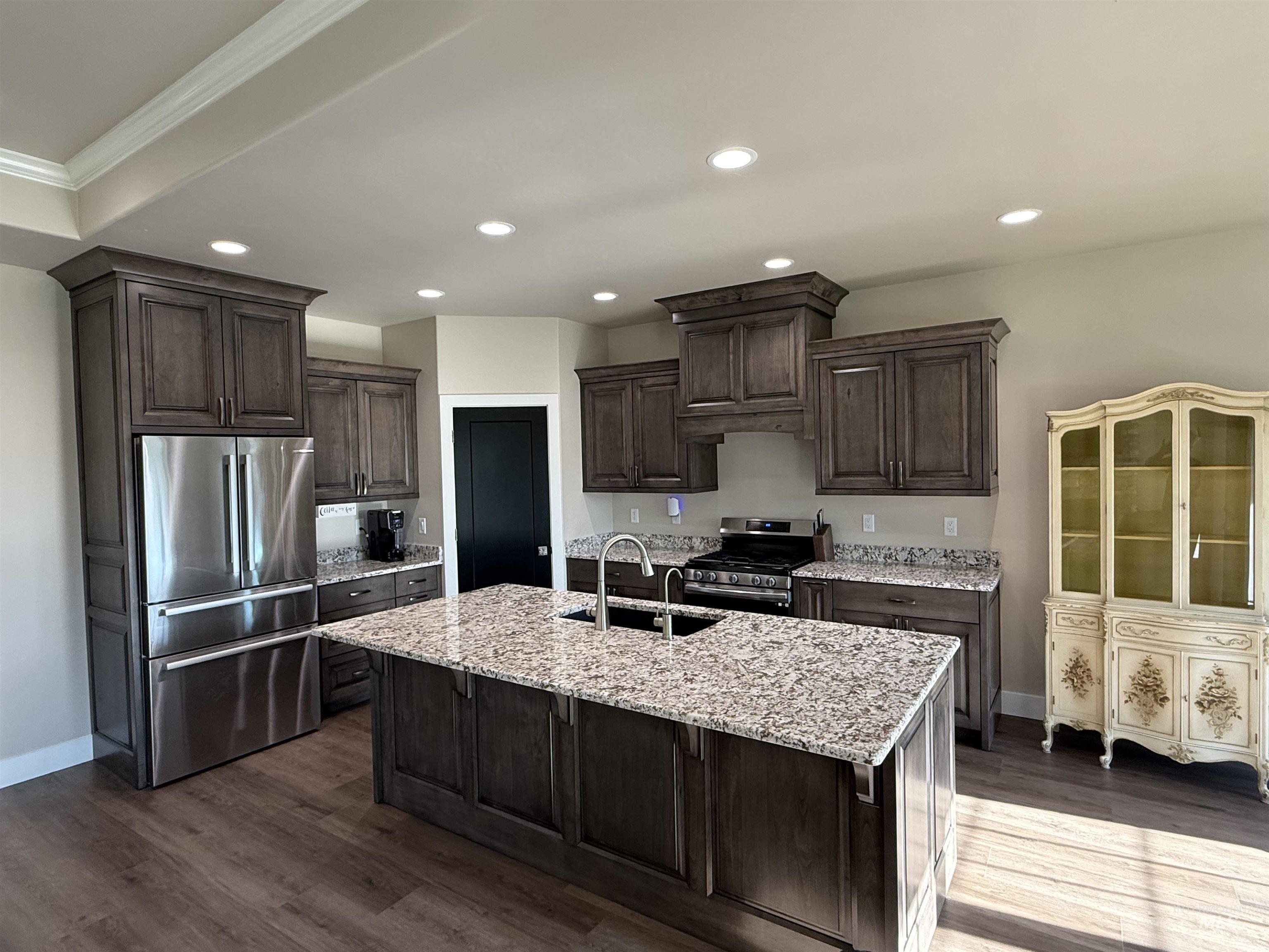Kitchen featuring dark brown cabinets, appliances with stainless steel finishes, light stone countertops, recessed lighting, and a kitchen island with sink