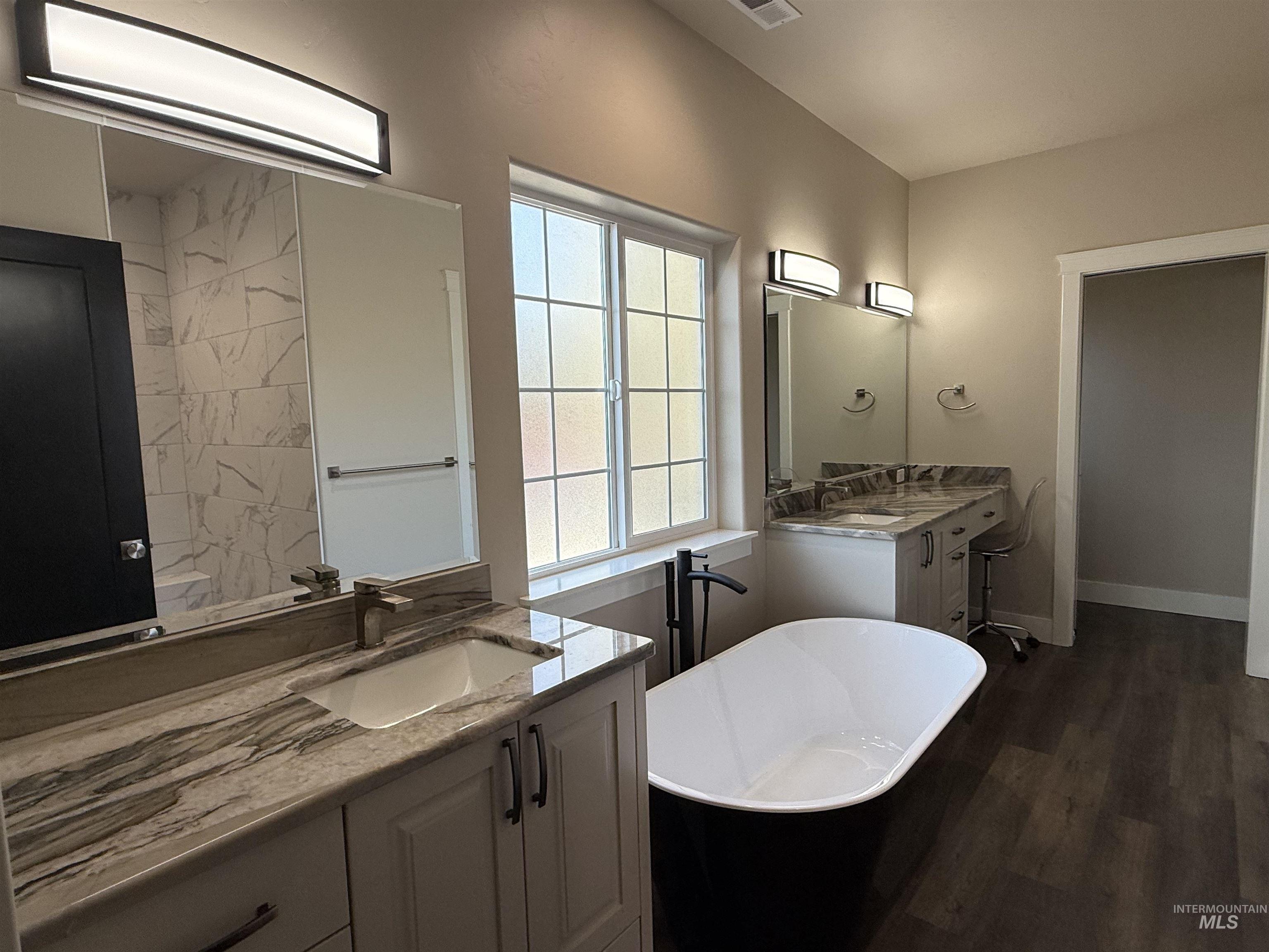 Full bath featuring a freestanding bath, two vanities, and dark wood finished floors