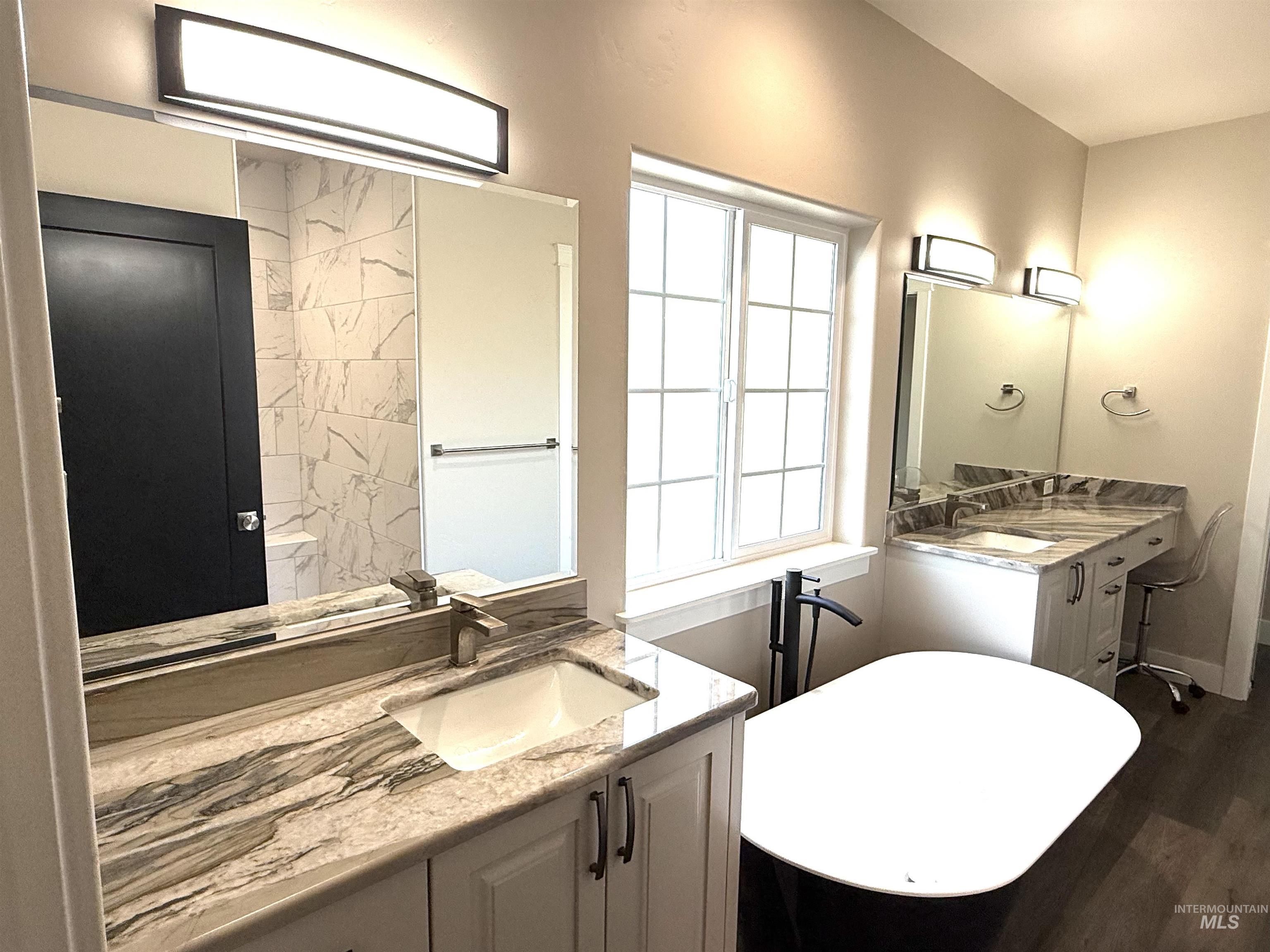 Full bath with a freestanding tub, two vanities, and dark wood-type flooring