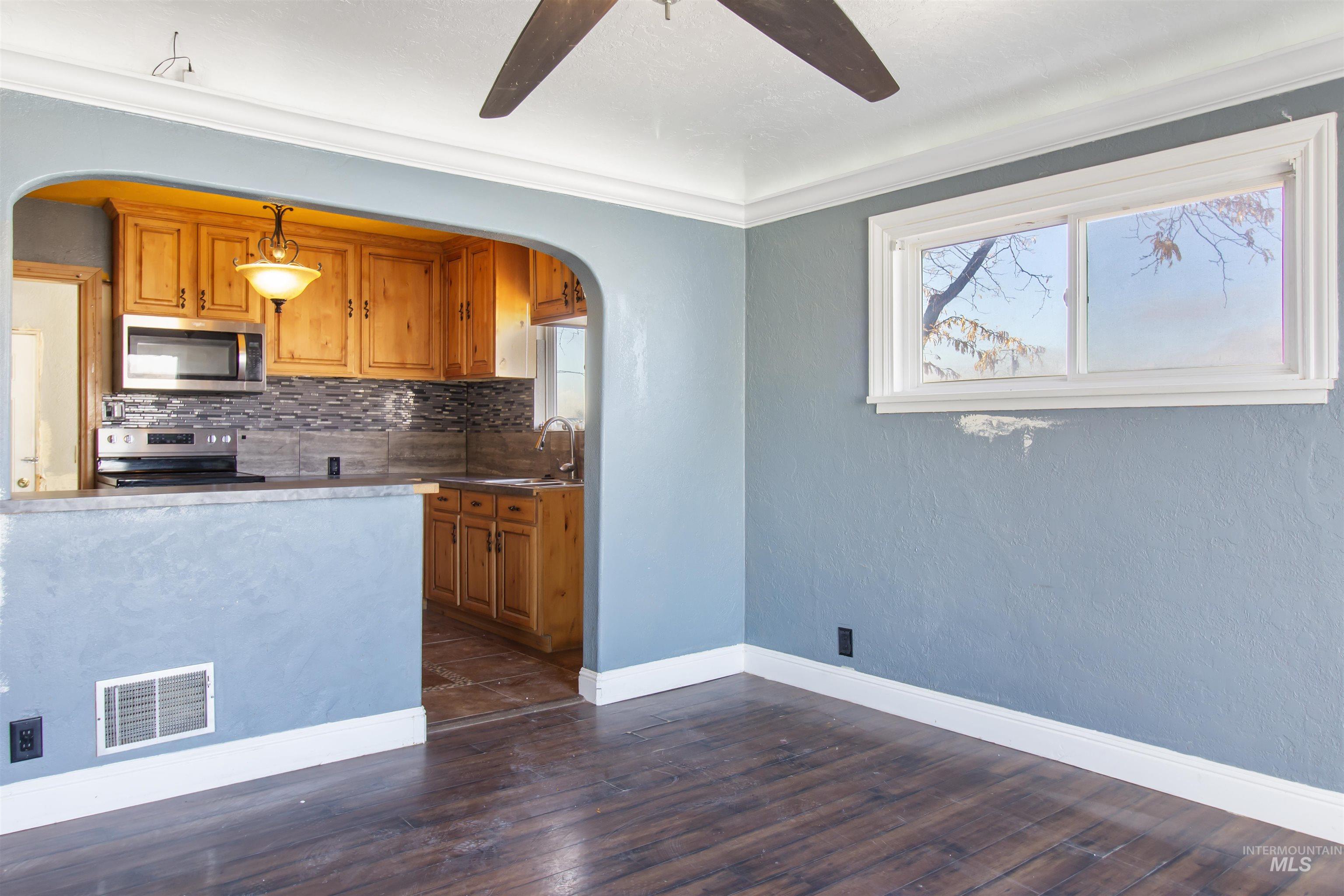 Kitchen featuring arched walkways, brown cabinetry, stainless steel appliances, backsplash, and crown molding