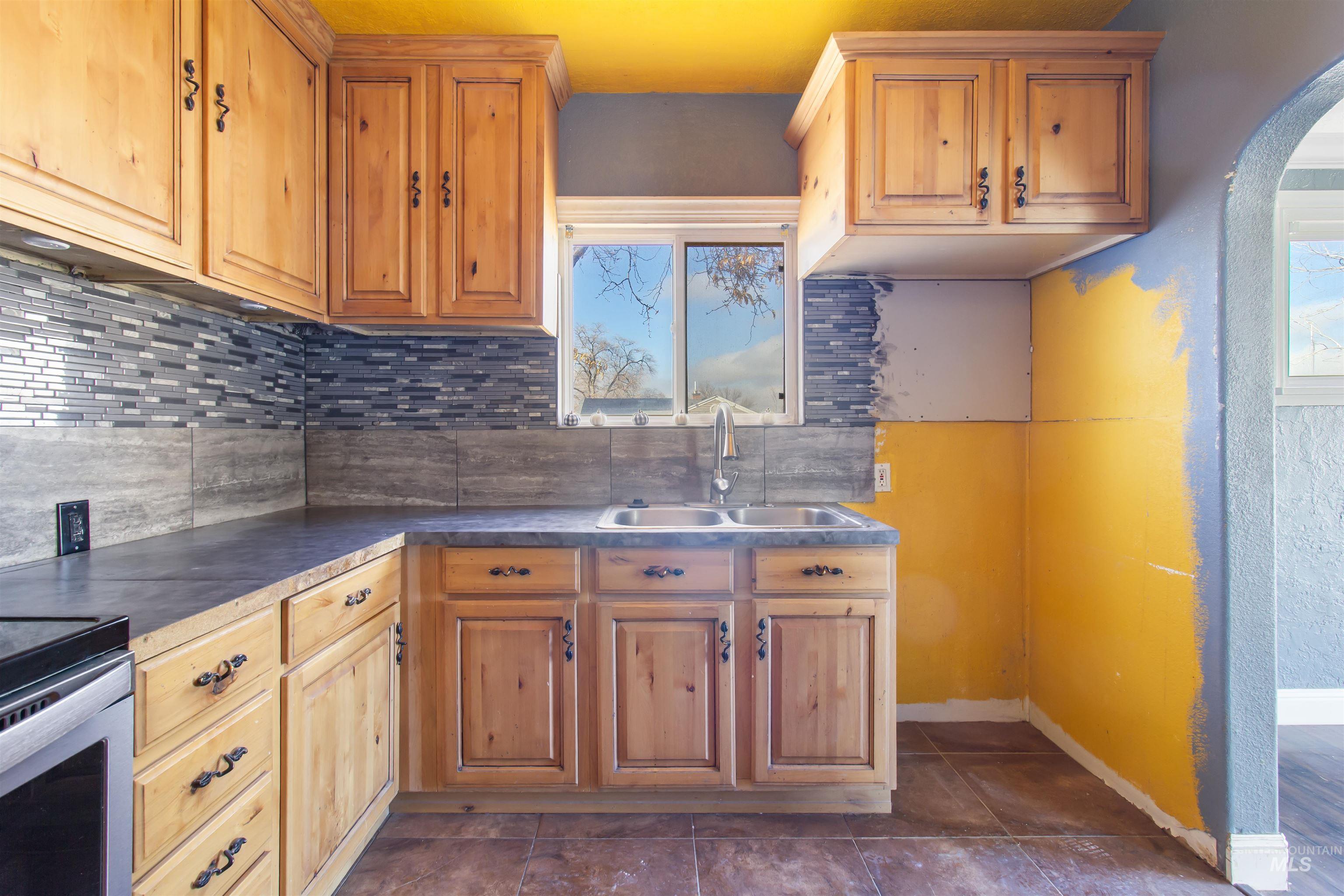 Kitchen featuring dark countertops, backsplash, arched walkways, stainless steel range oven, and dark tile patterned floors