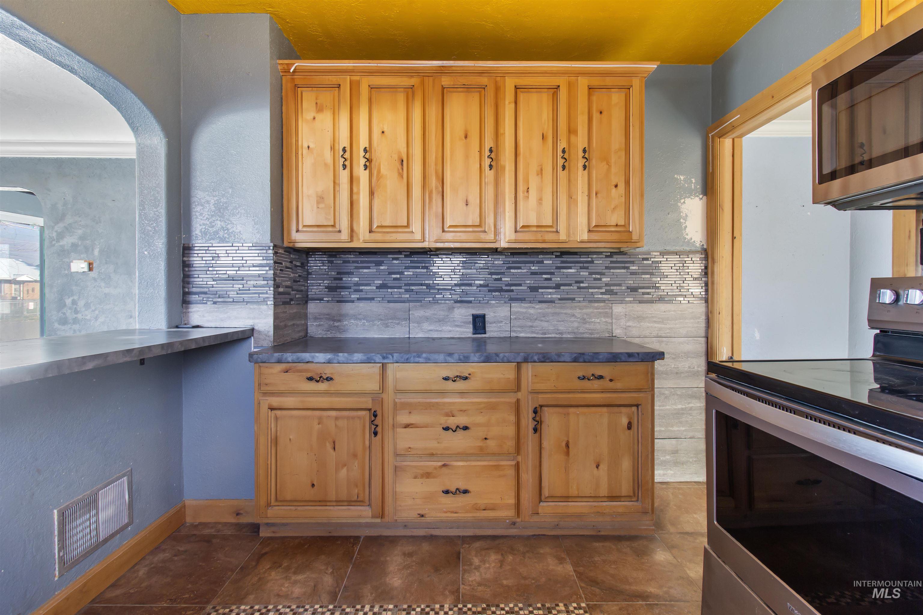 Kitchen with appliances with stainless steel finishes, arched walkways, a textured wall, and tasteful backsplash