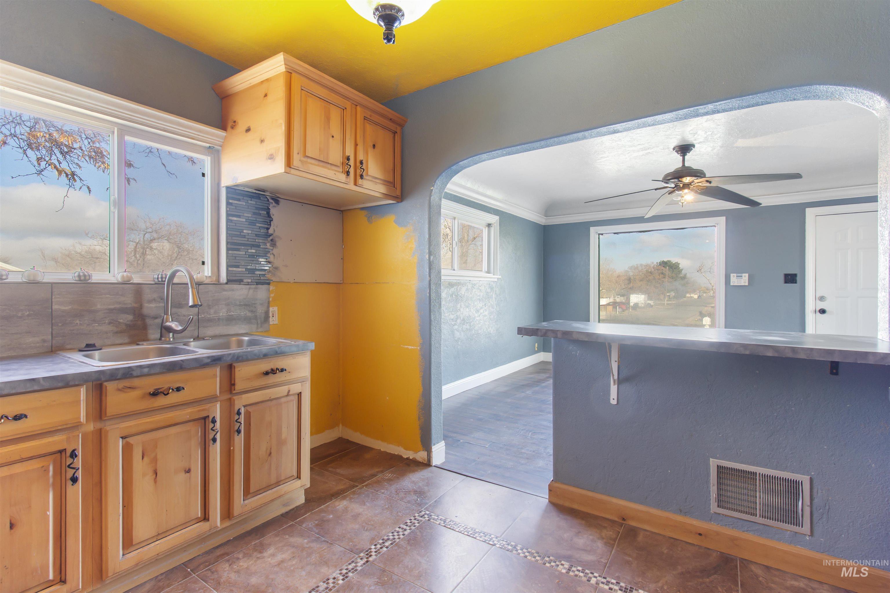 Kitchen with ceiling fan, dark tile patterned floors, crown molding, arched walkways, and decorative backsplash
