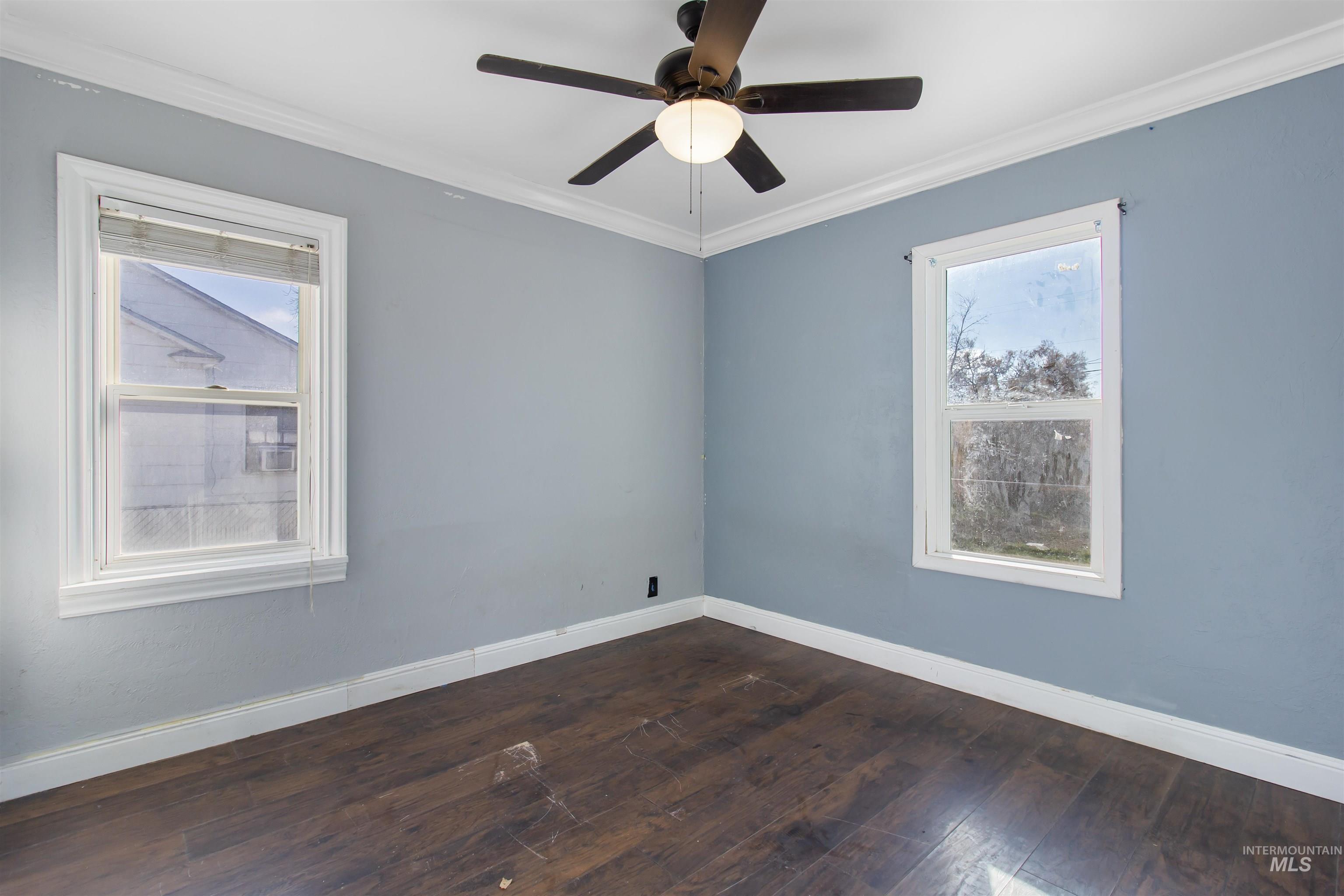 Empty room featuring crown molding, dark wood-style floors, plenty of natural light, and a ceiling fan