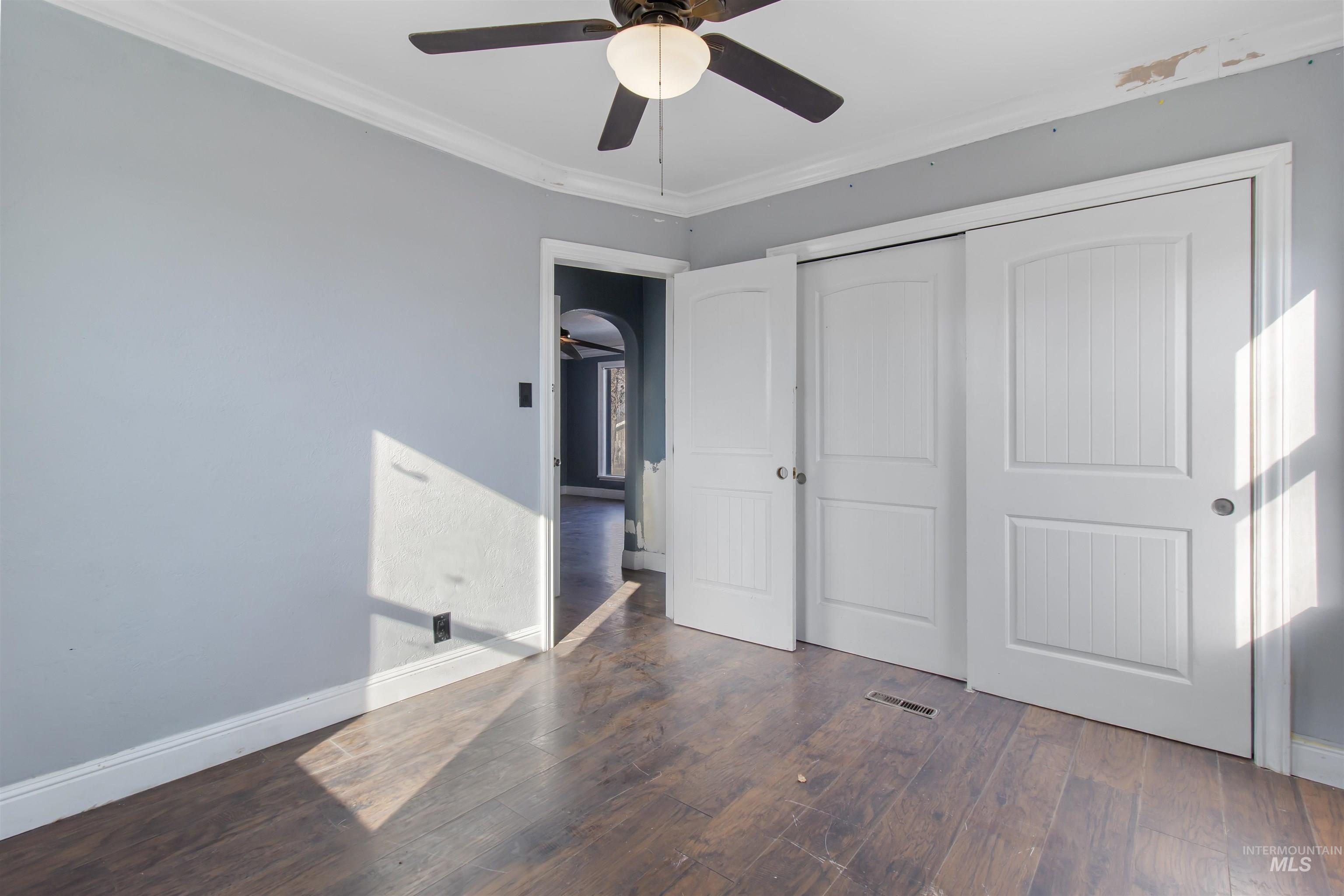 Unfurnished bedroom featuring ornamental molding, dark wood finished floors, a closet, and a ceiling fan