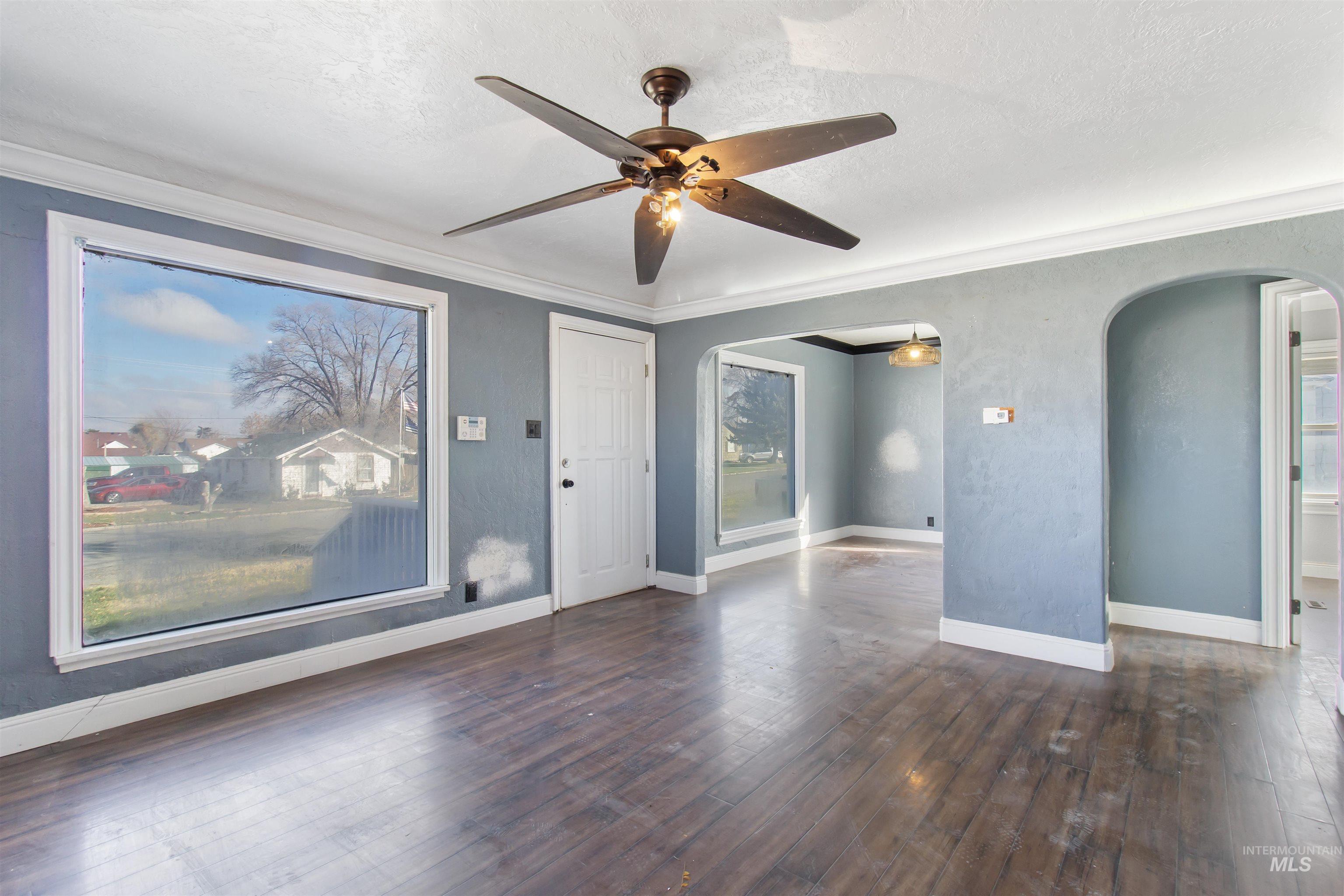 Unfurnished room with dark wood finished floors, ceiling fan, ornamental molding, a textured ceiling, and a textured wall