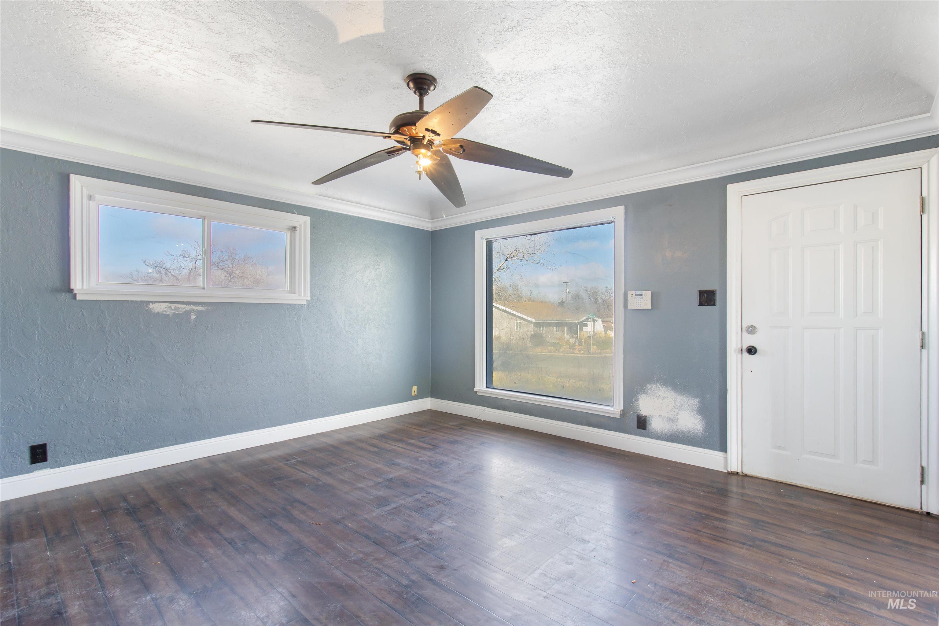 Unfurnished room featuring dark wood-type flooring, crown molding, a textured ceiling, ceiling fan, and a textured wall