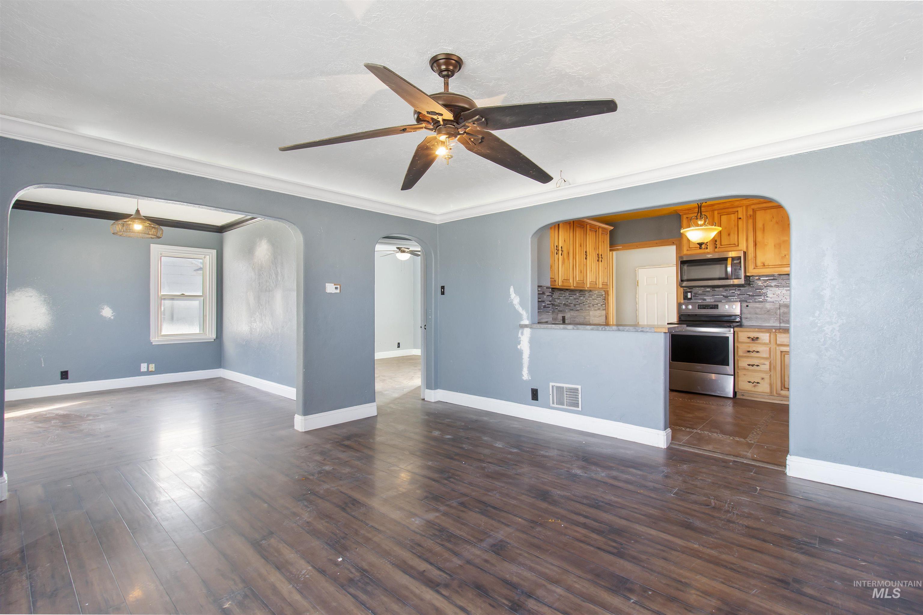 Unfurnished living room with arched walkways, ceiling fan, crown molding, and dark wood-type flooring