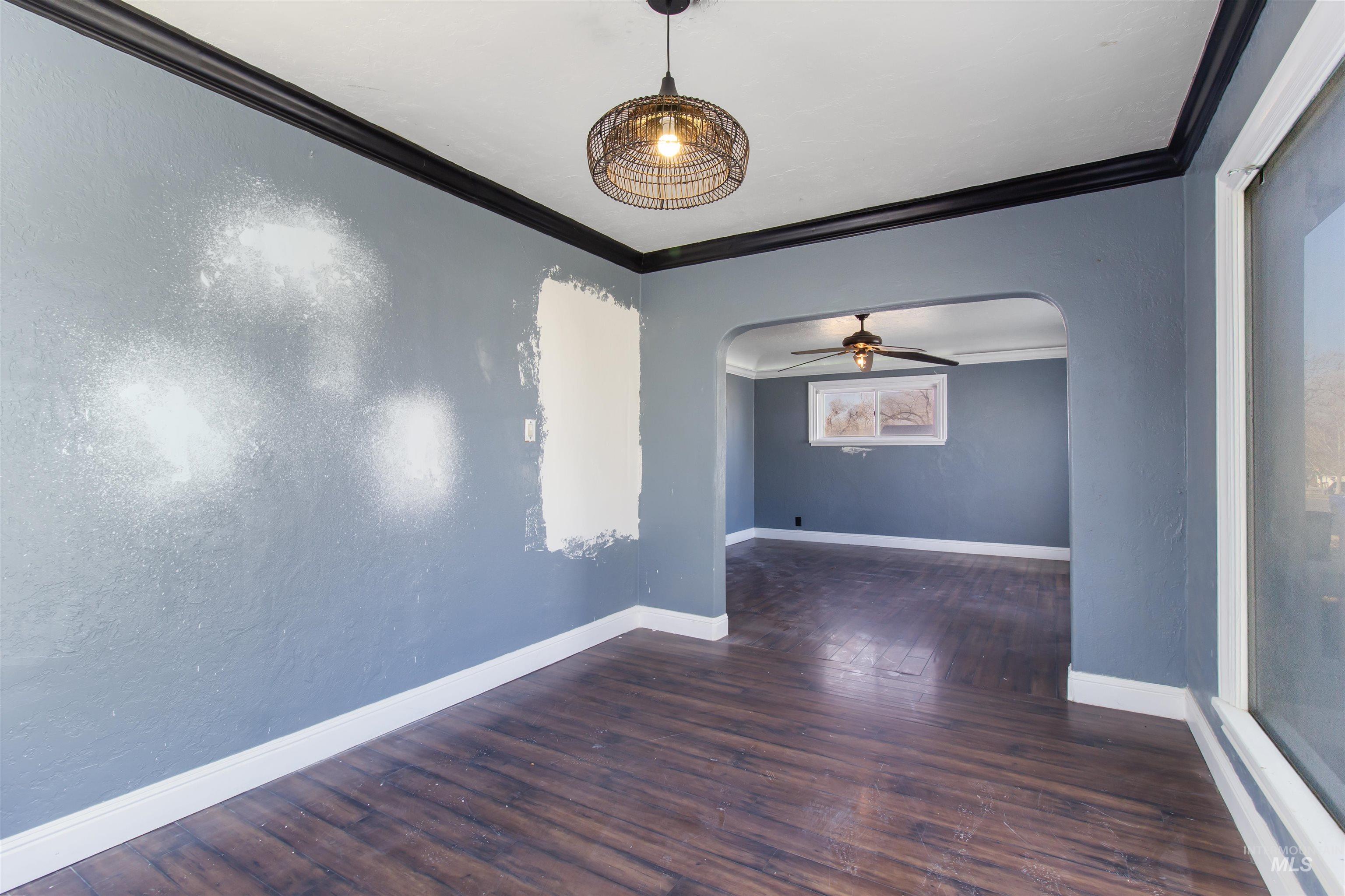 Empty room with arched walkways, crown molding, dark wood-type flooring, ceiling fan, and a textured wall