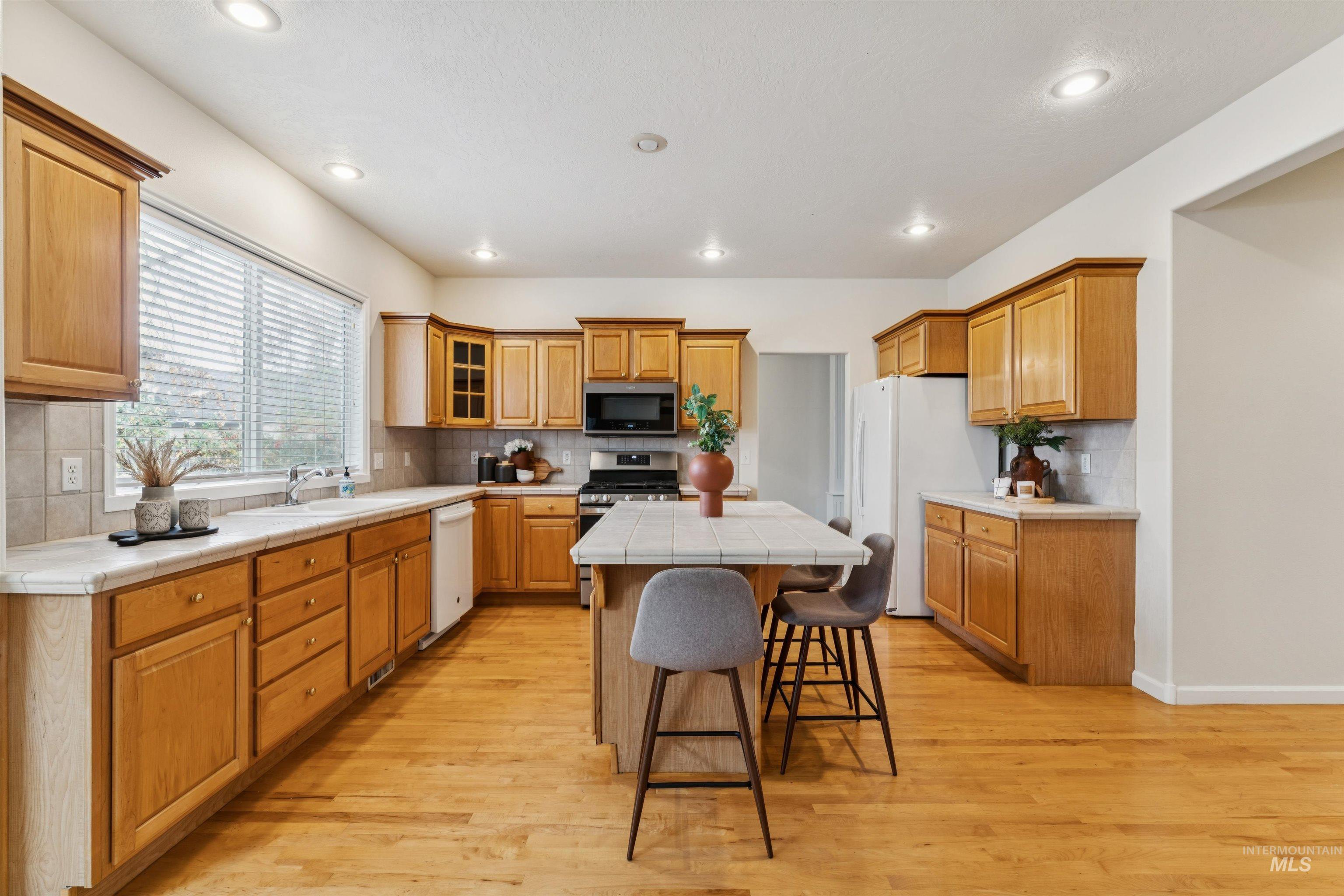 Kitchen with tile counters, a kitchen bar, stainless steel appliances, a kitchen island, and backsplash