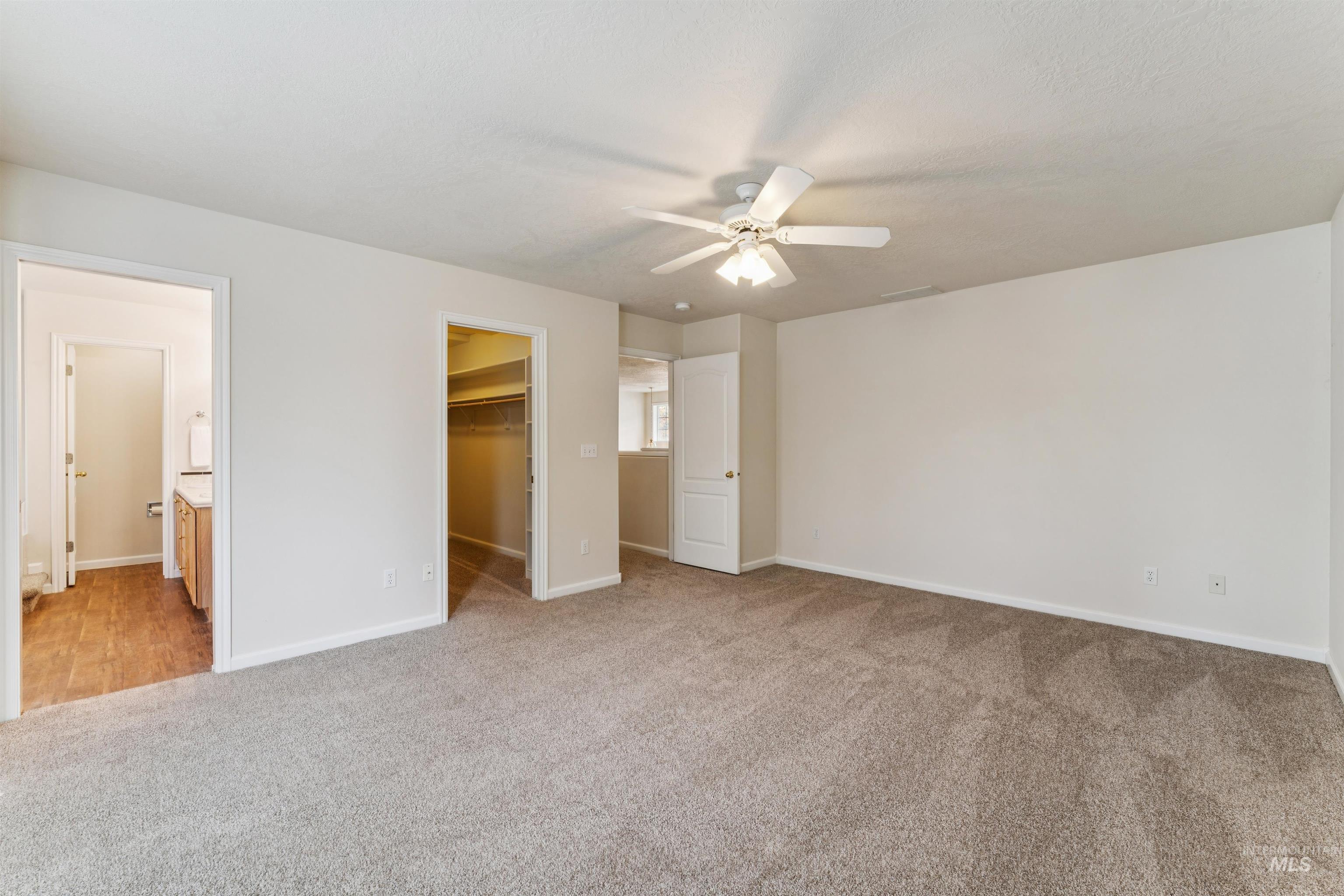Unfurnished bedroom with a walk in closet, light colored carpet, a ceiling fan, and ensuite bath
