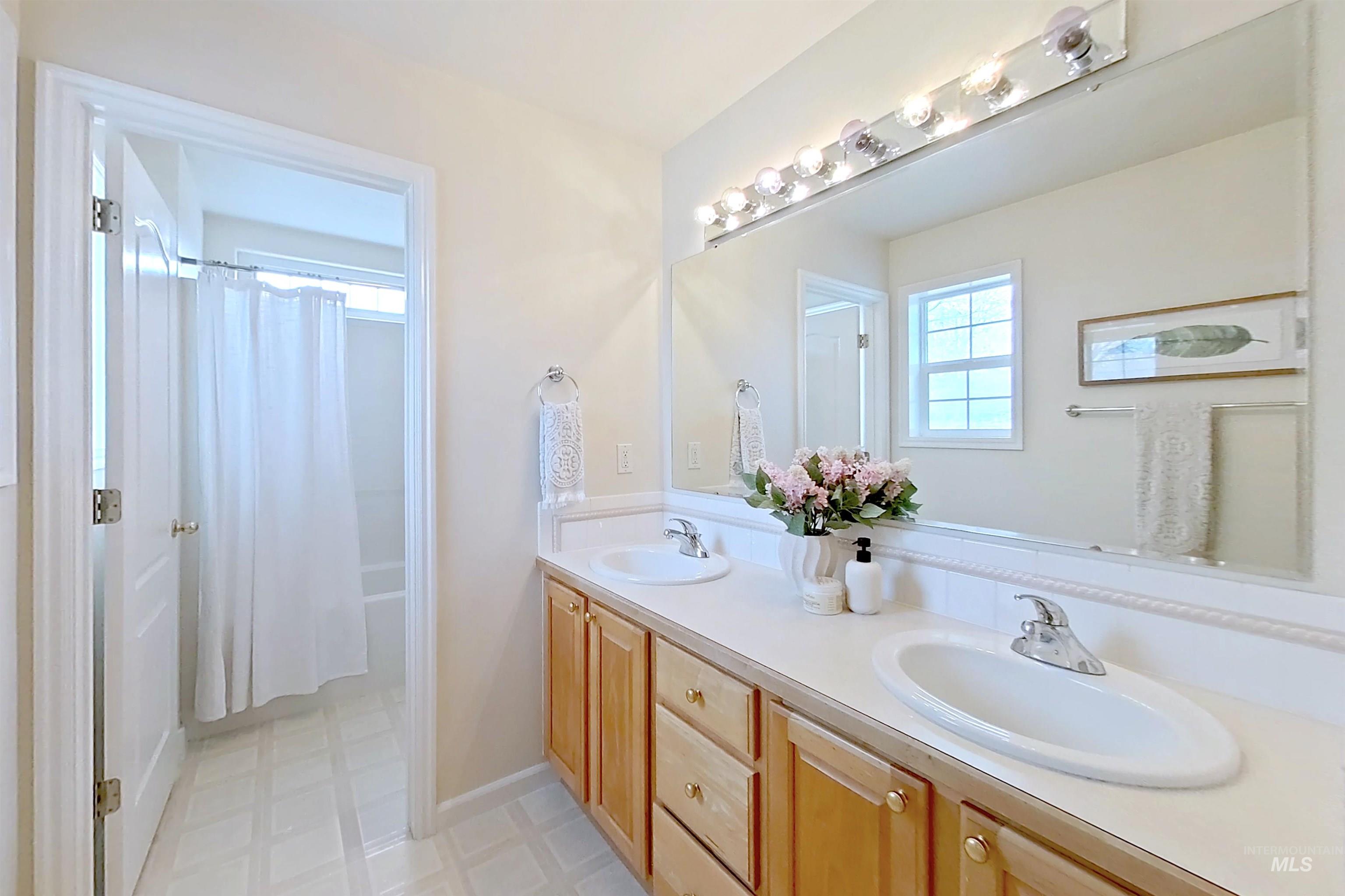 Bathroom featuring double vanity, healthy amount of natural light, shower / bath combo with shower curtain, and light flooring