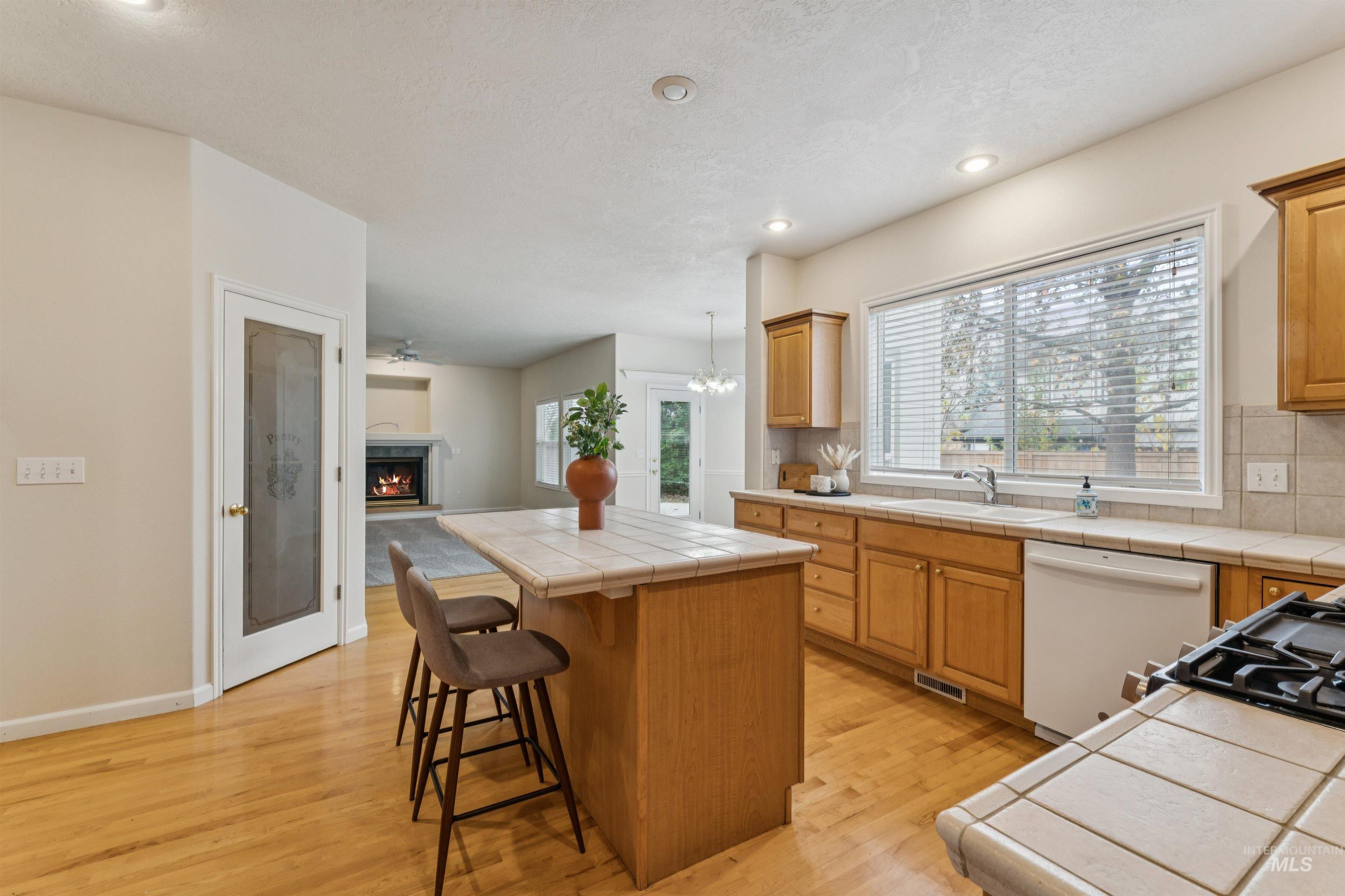 Kitchen featuring a warm lit fireplace, tile counters, a breakfast bar, a center island, and white dishwasher