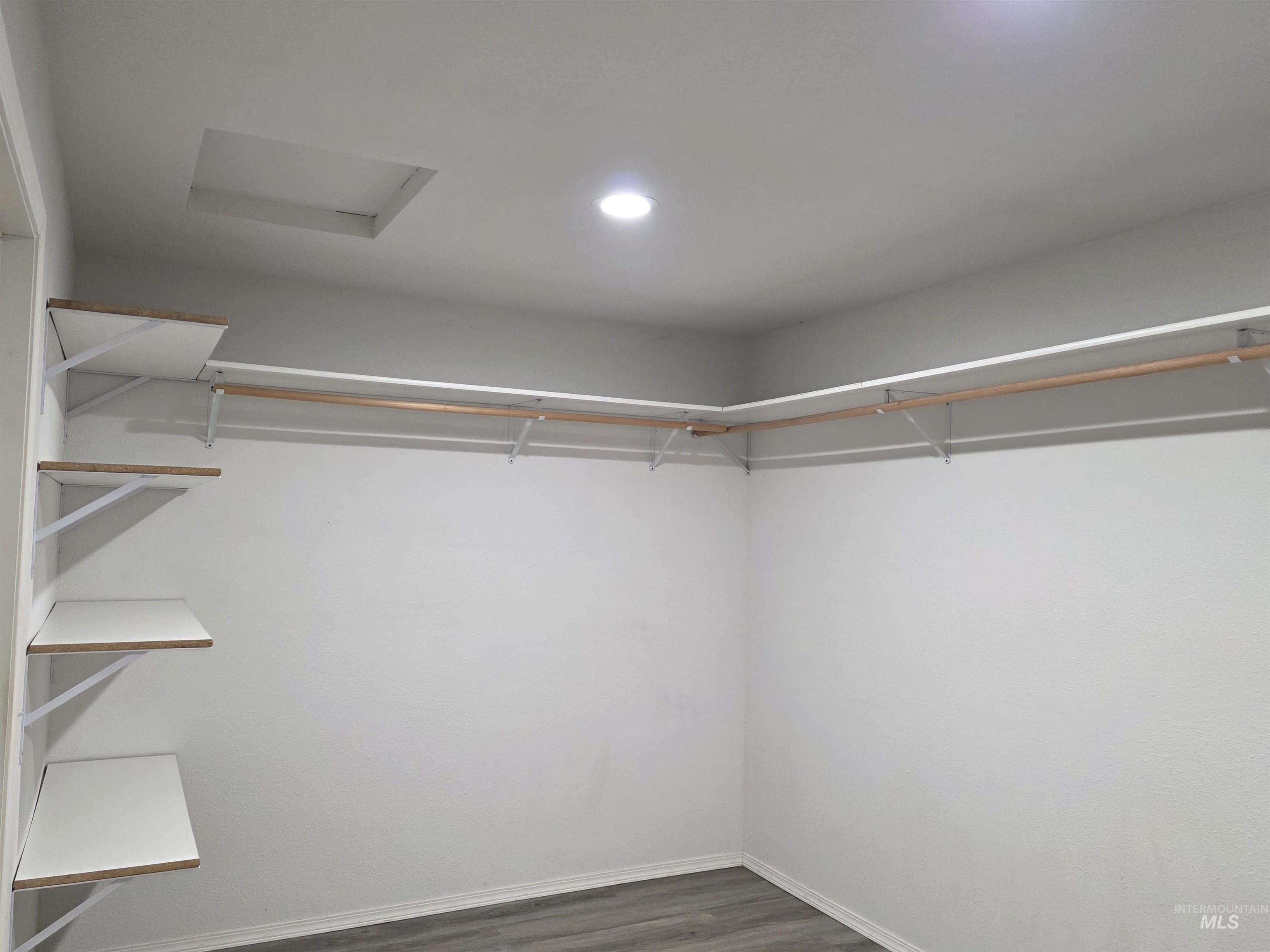 Walk in closet featuring attic access and dark wood-style floors