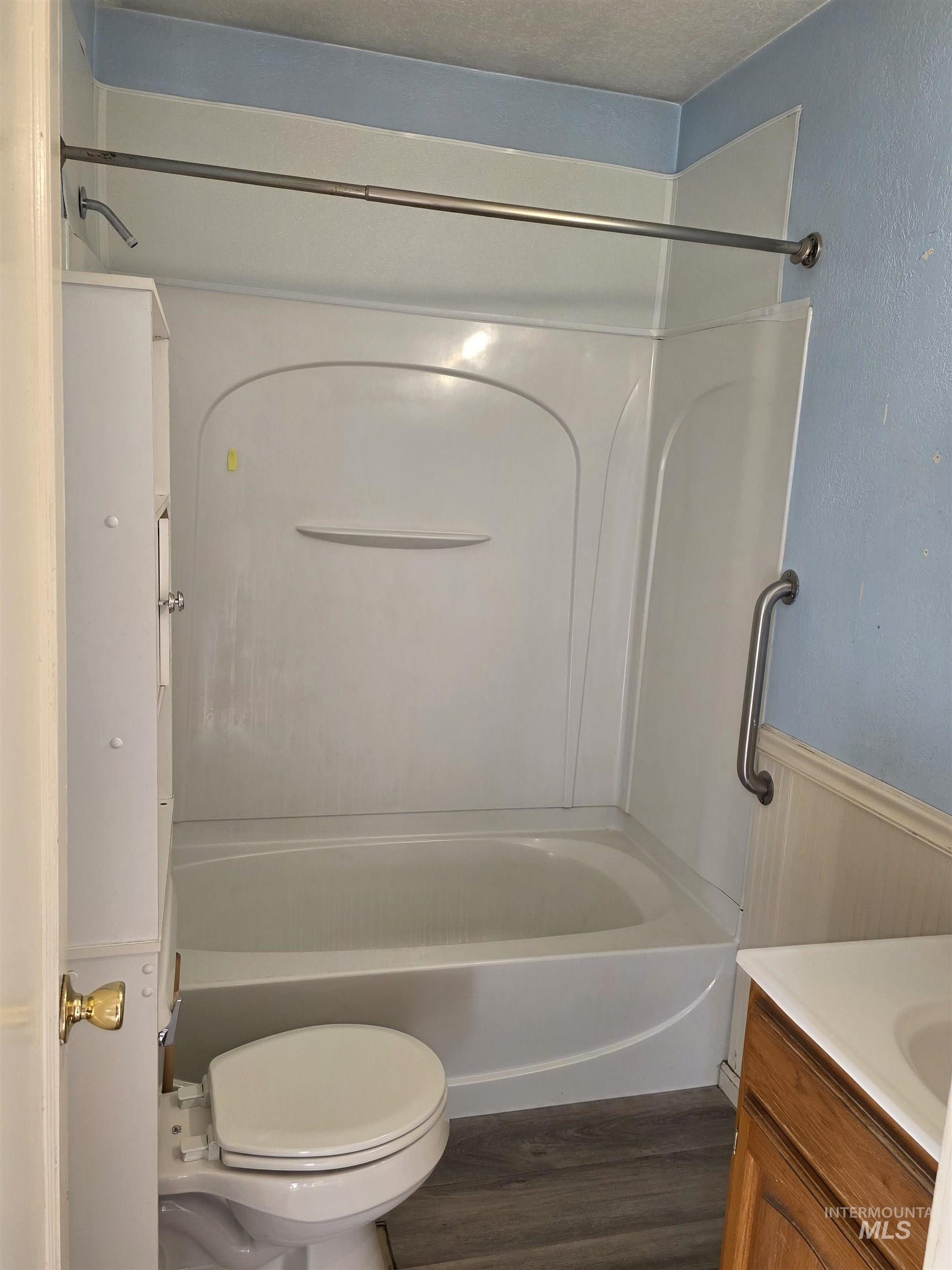 Bathroom with vanity, shower / bath combination, dark wood-style floors, and wainscoting