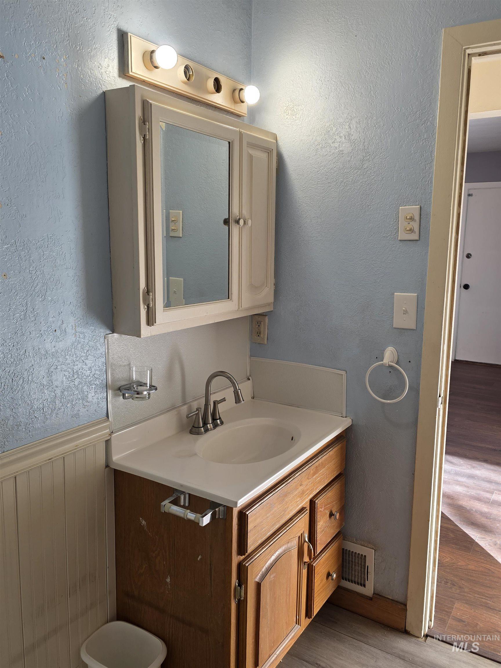 Half bath featuring a textured wall, vanity, wainscoting, and wood finished floors