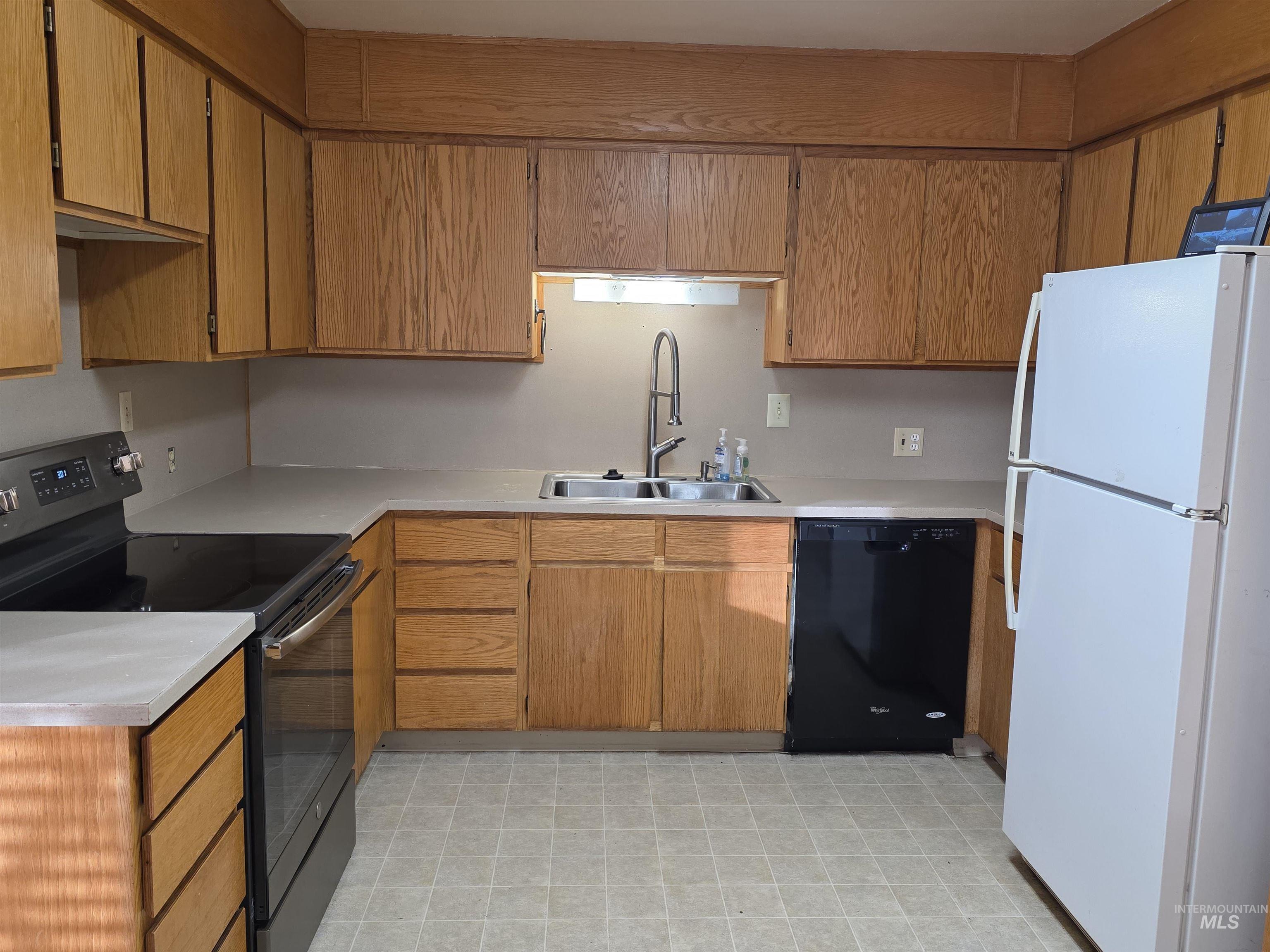Kitchen featuring black appliances, light countertops, light flooring, and brown cabinetry