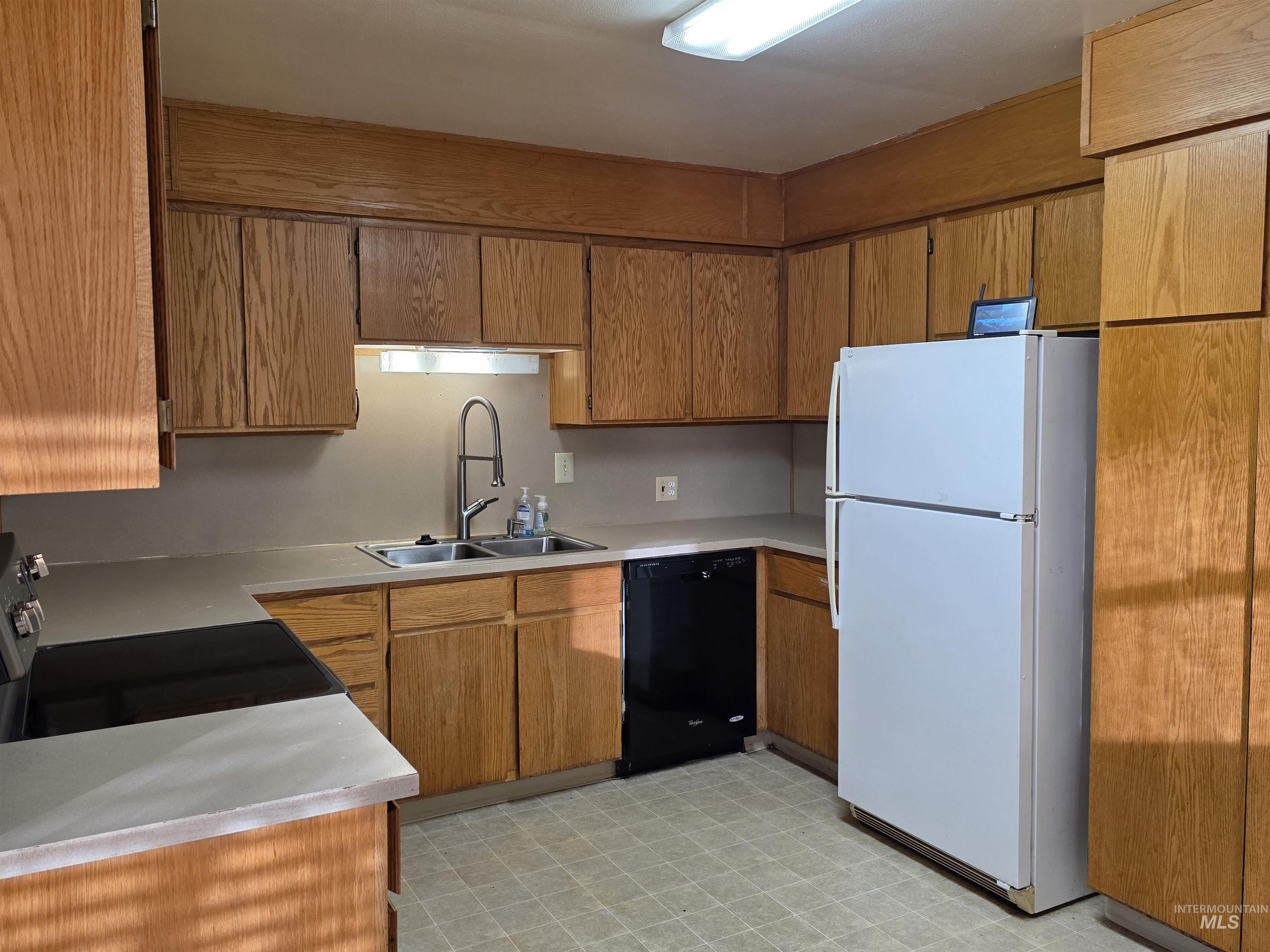 Kitchen with freestanding refrigerator, light floors, brown cabinetry, light countertops, and dishwasher