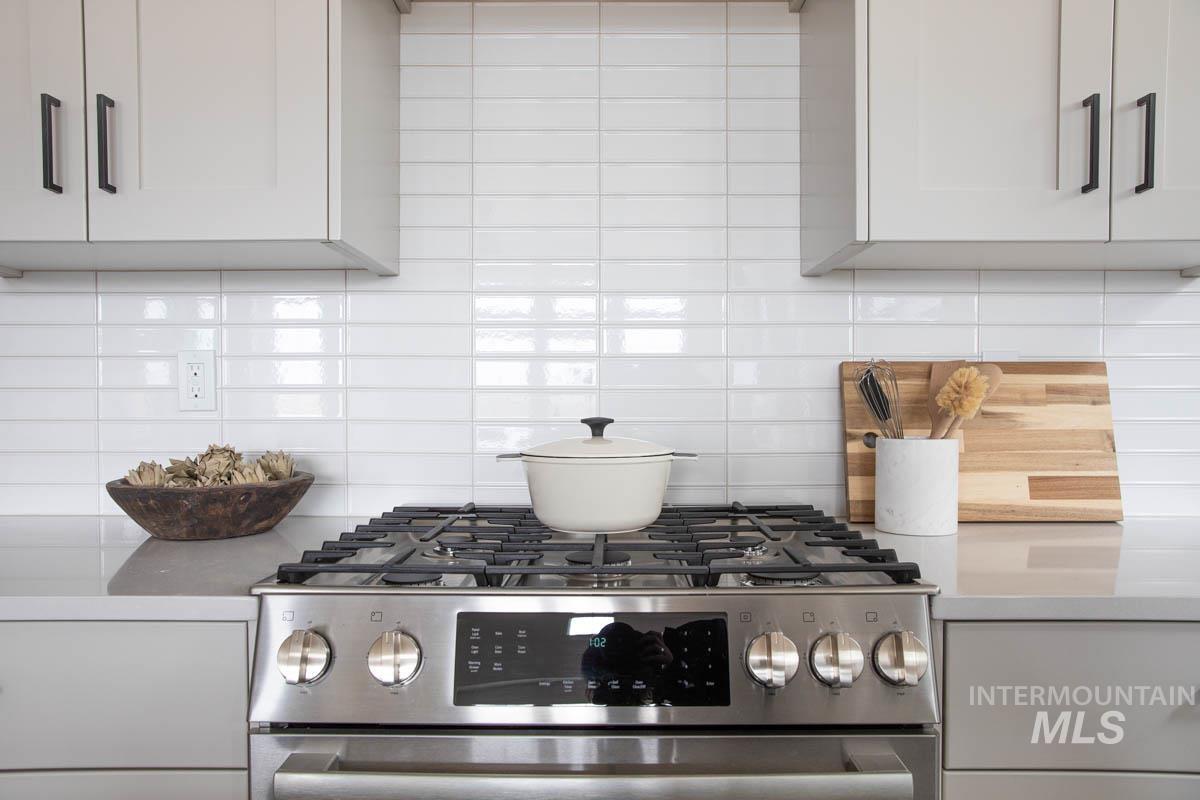 Kitchen view of stainless steel range with gas cooktop, decorative backsplash, white cabinets, and light stone counters